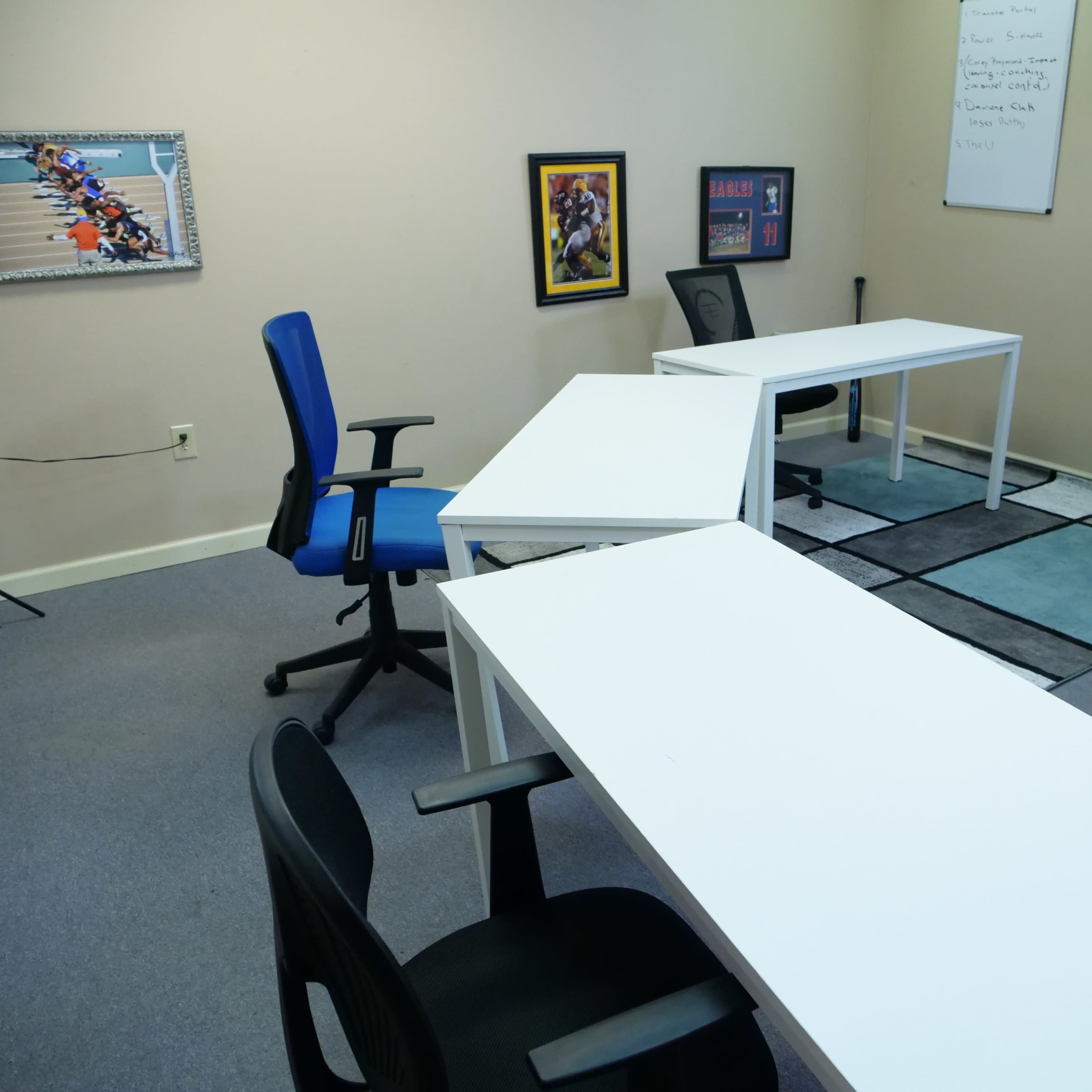 A sparsely furnished office space with three white desks arranged in a U-shape, two chairs, and a whiteboard on the wall.