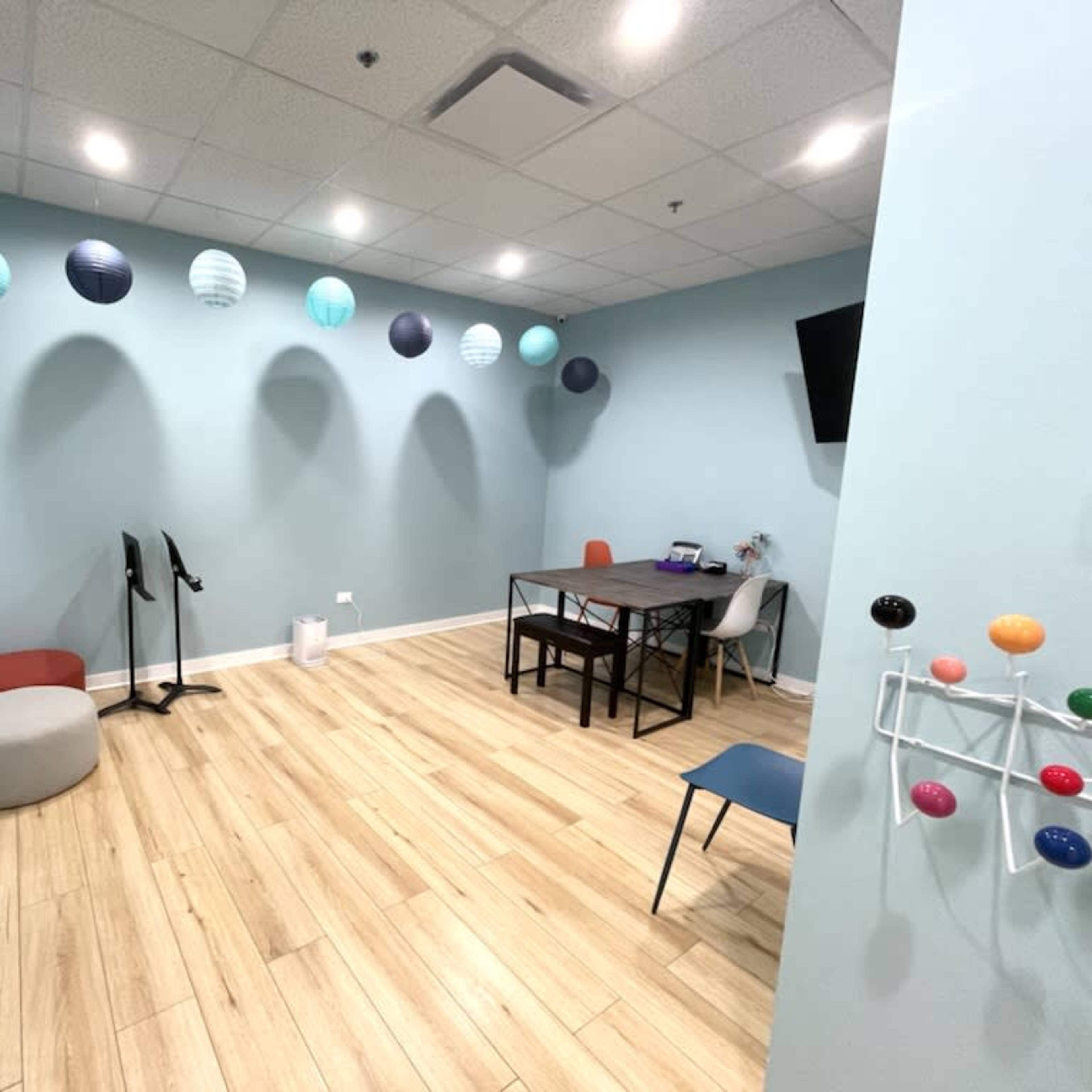 A light blue room with wooden flooring, featuring a table, chairs, and decorative paper lanterns hanging from the ceiling.