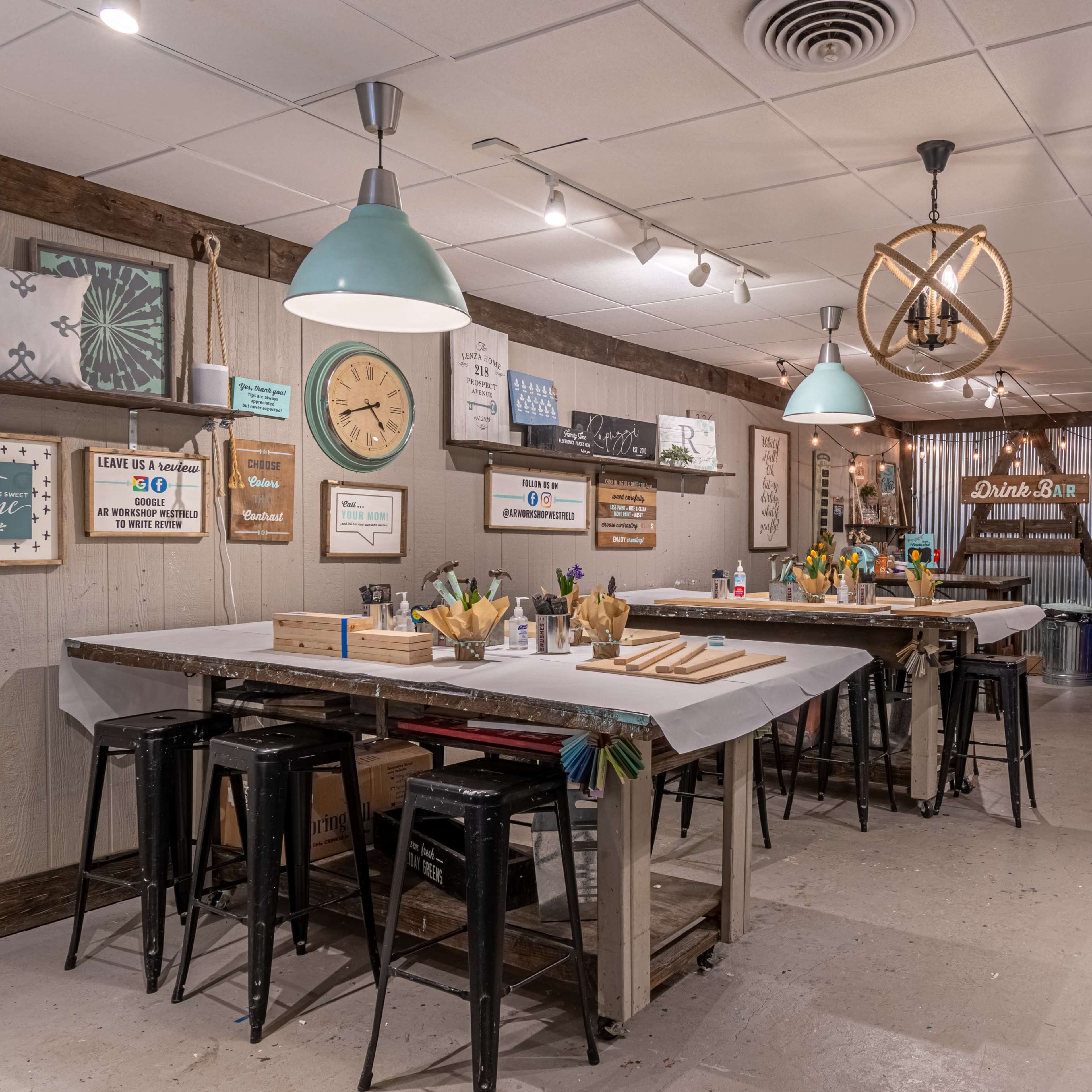 An art studio with multiple work tables, pendant lighting, and supplies organized for creative activities.