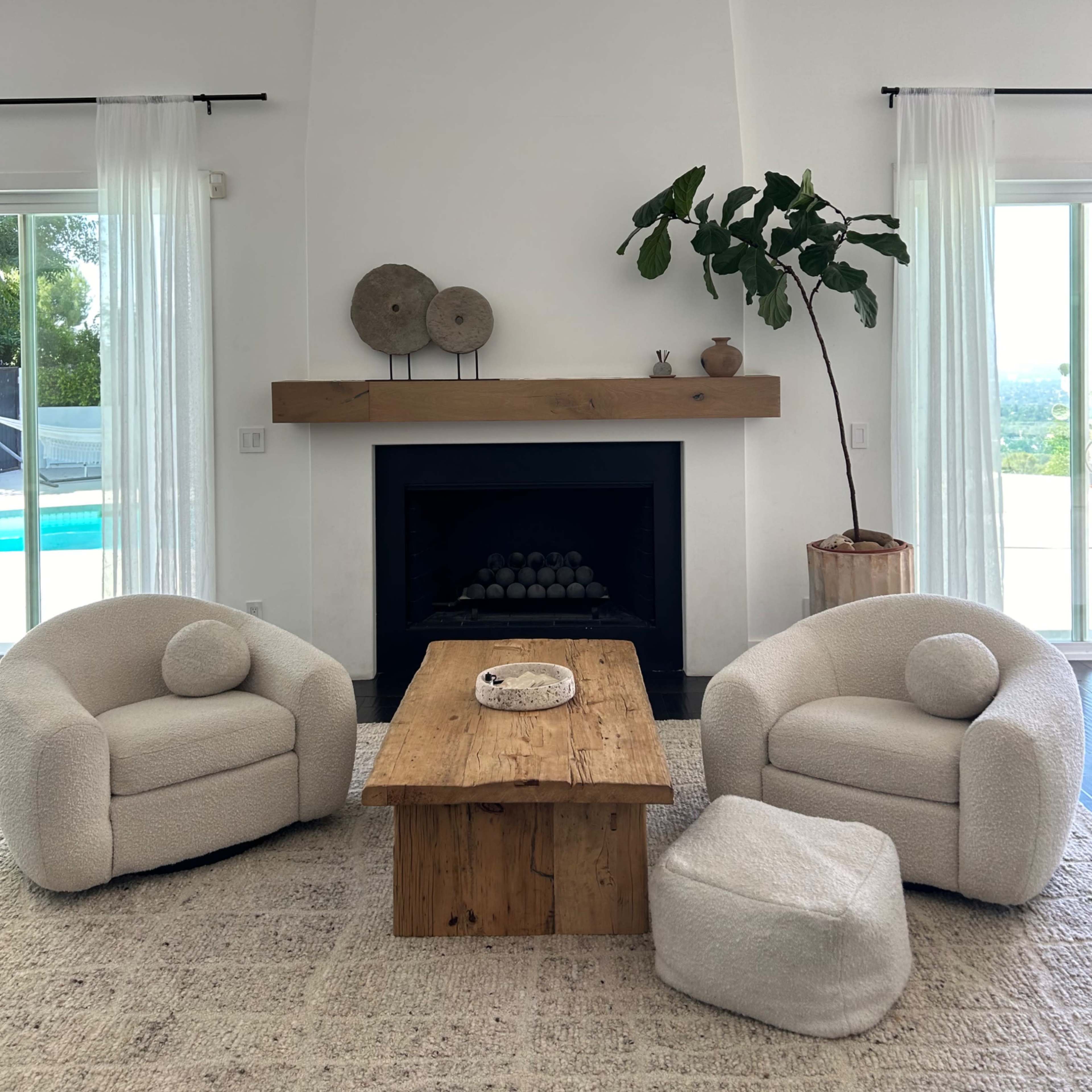 A modern living room featuring two upholstered chairs, a wooden coffee table, and a fireplace with decorative items on the mantel.