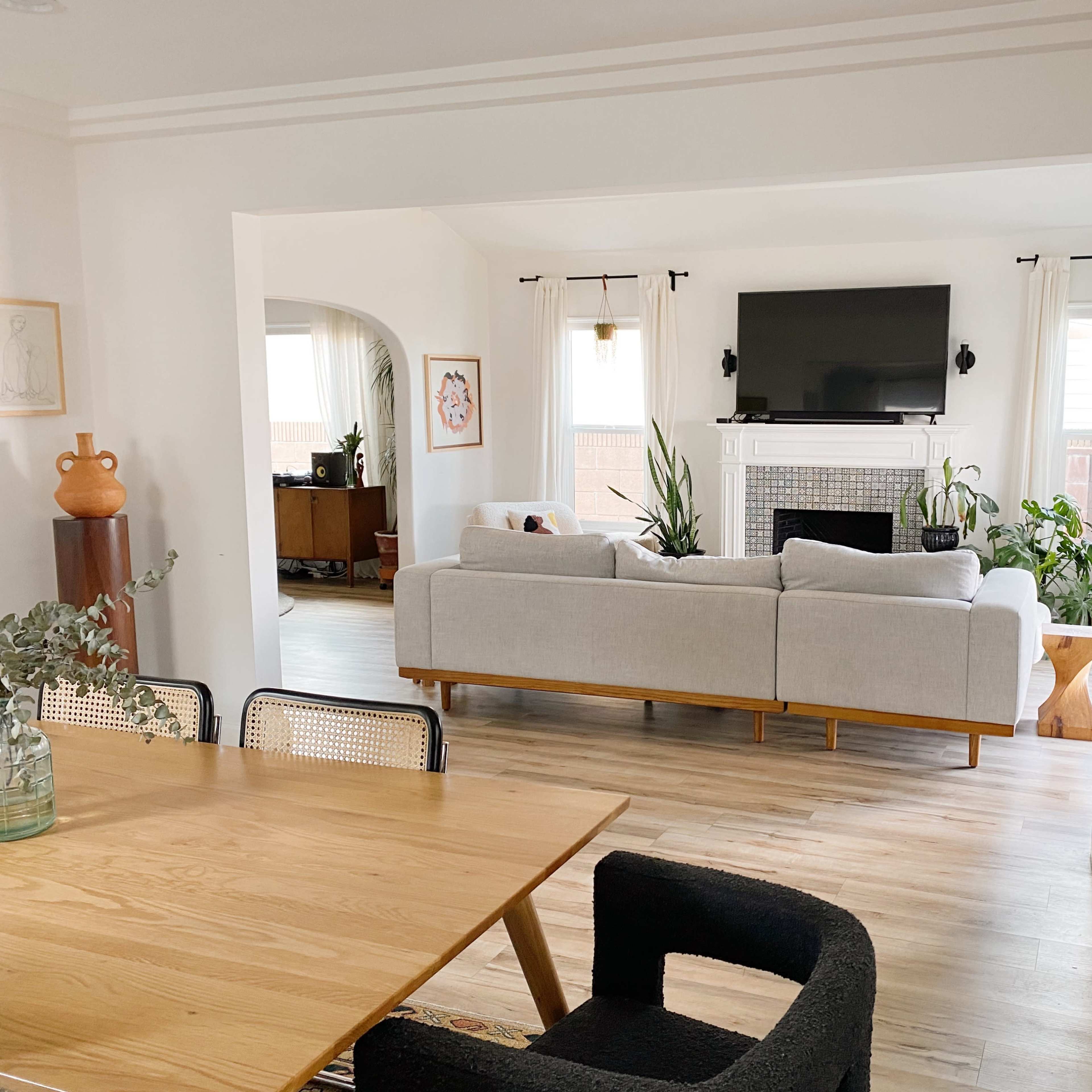 A living area features a light-colored sectional sofa facing a television, with plants and wood accents in a spacious, open layout.