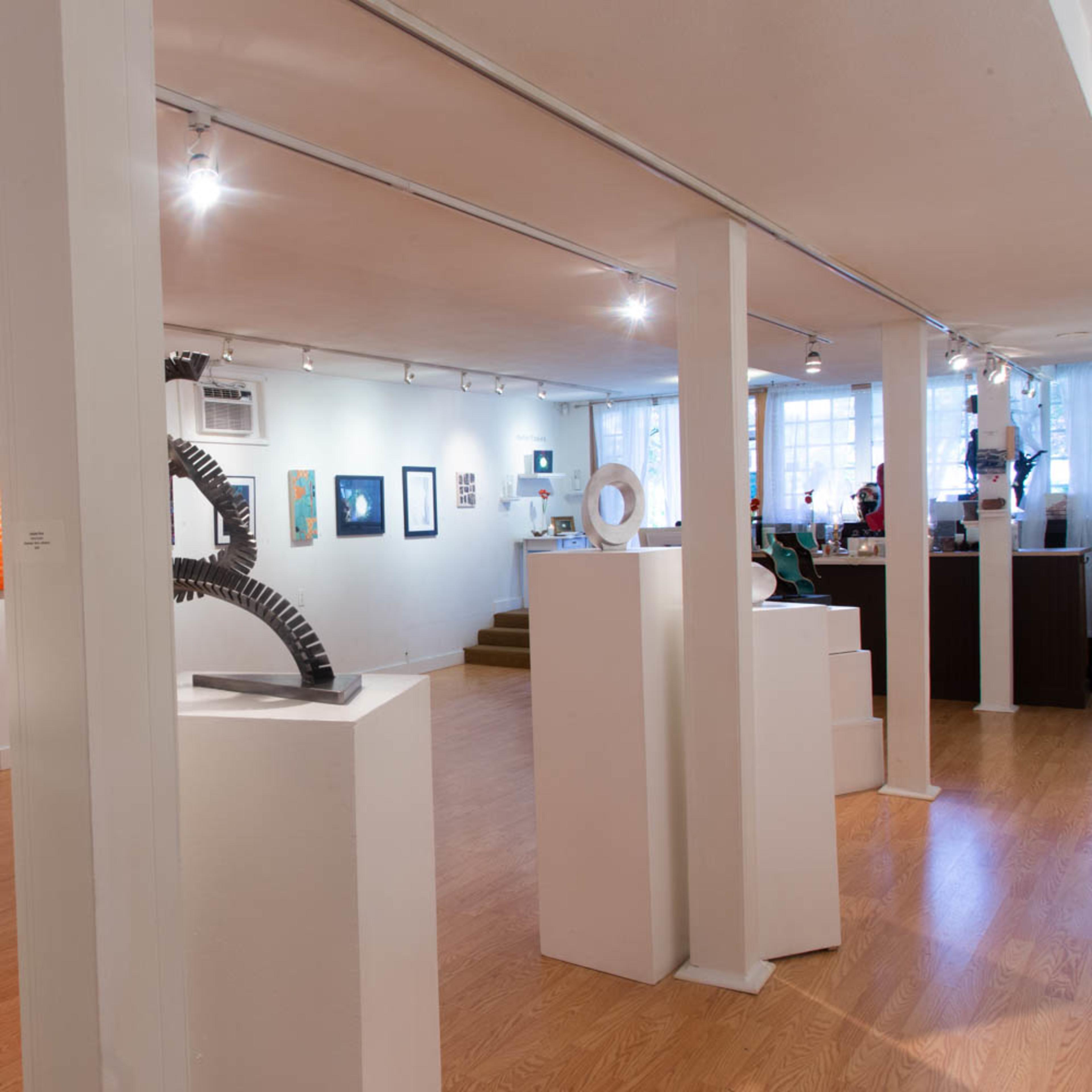 A spacious art gallery featuring various sculptures and paintings displayed on white walls and pedestals.