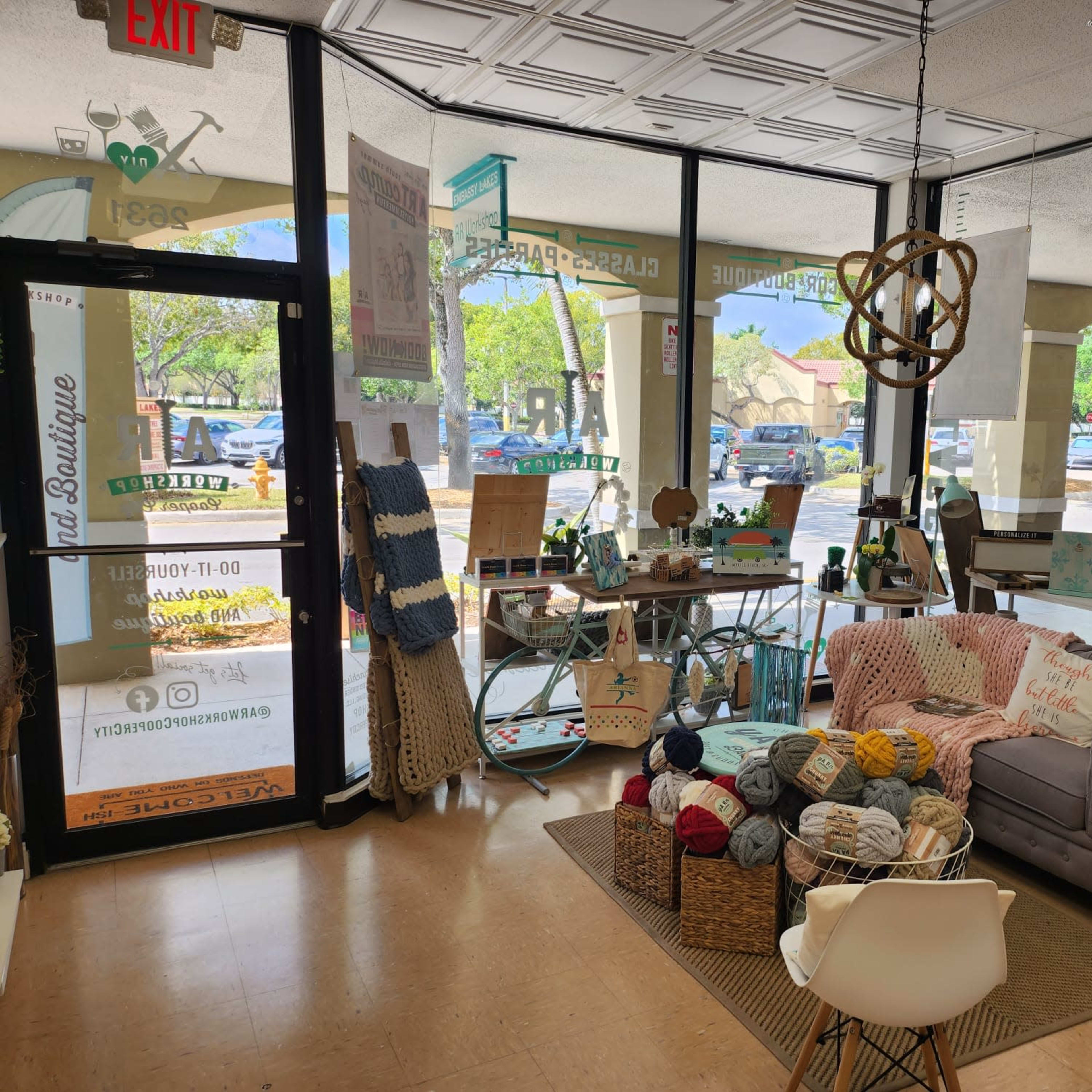 A craft boutique with a cozy seating area, various handmade items displayed, and bright natural light streaming through large windows.