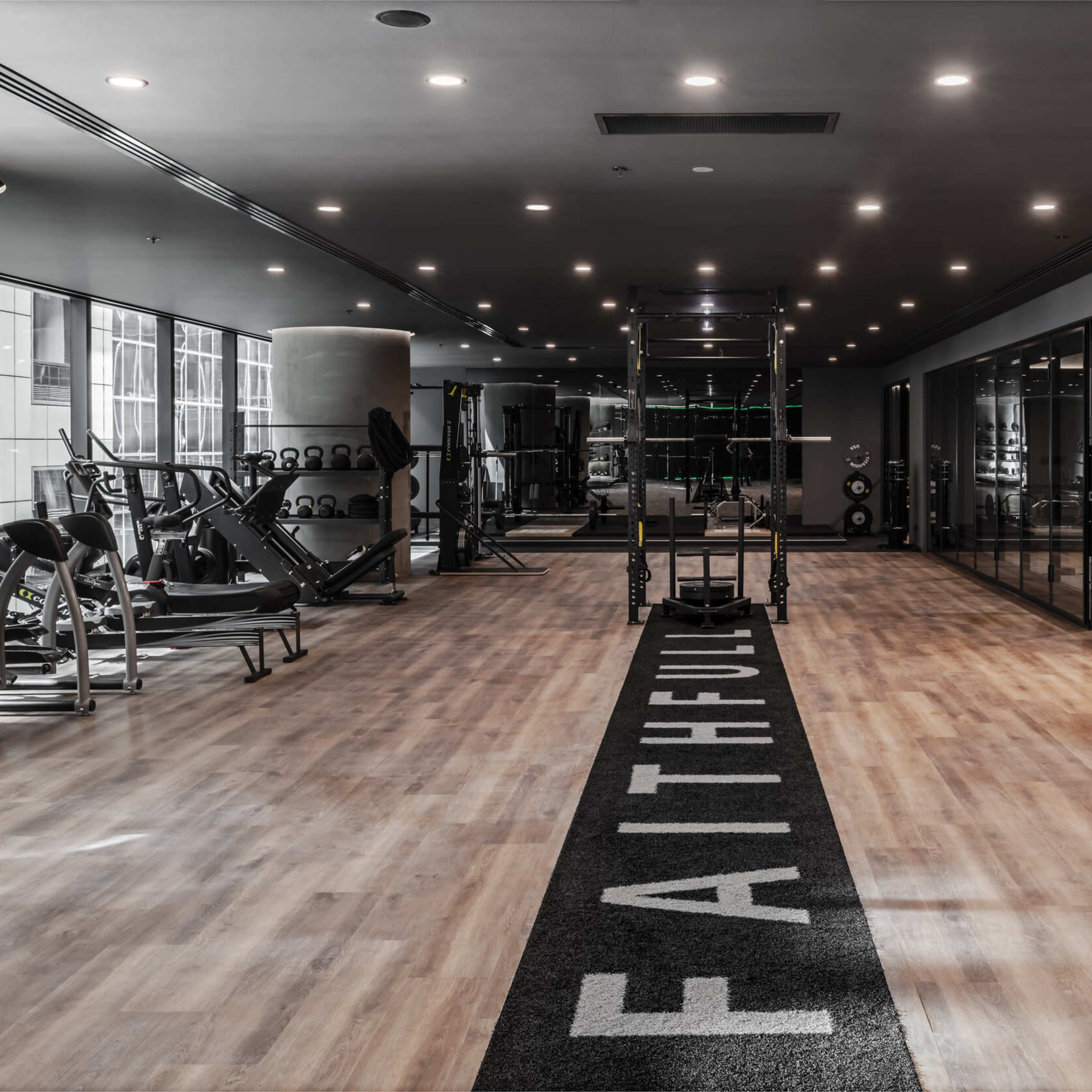 A modern gym features wooden flooring, workout equipment on one side, and a wall adorned with greenery and a fitness area.