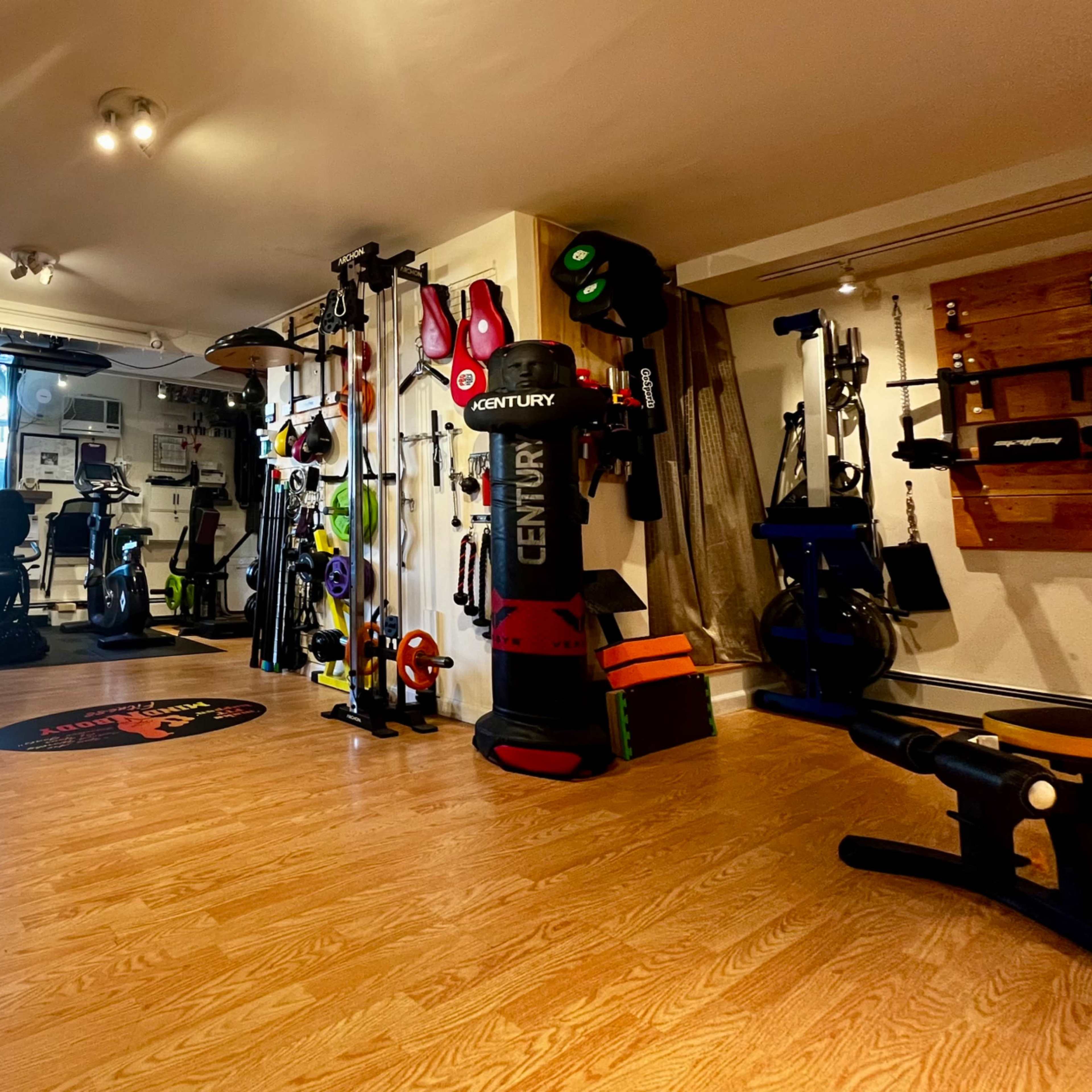 A well-equipped gym space featuring various fitness equipment, including dumbbells, exercise machines, and training tools, arranged neatly in a brightly lit room.