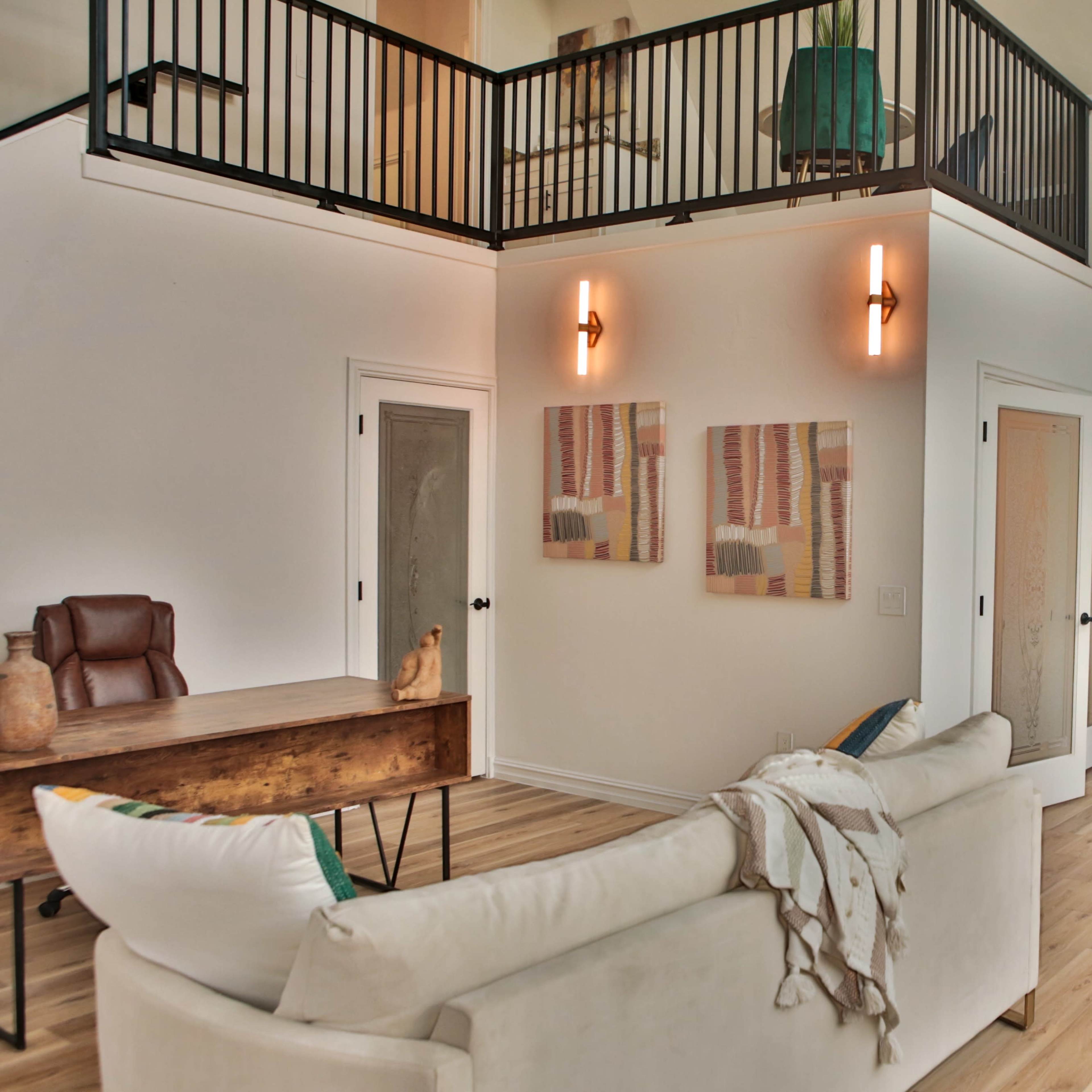 A modern living room with a high ceiling, featuring a sofa, a wooden table, and a small kitchen area.