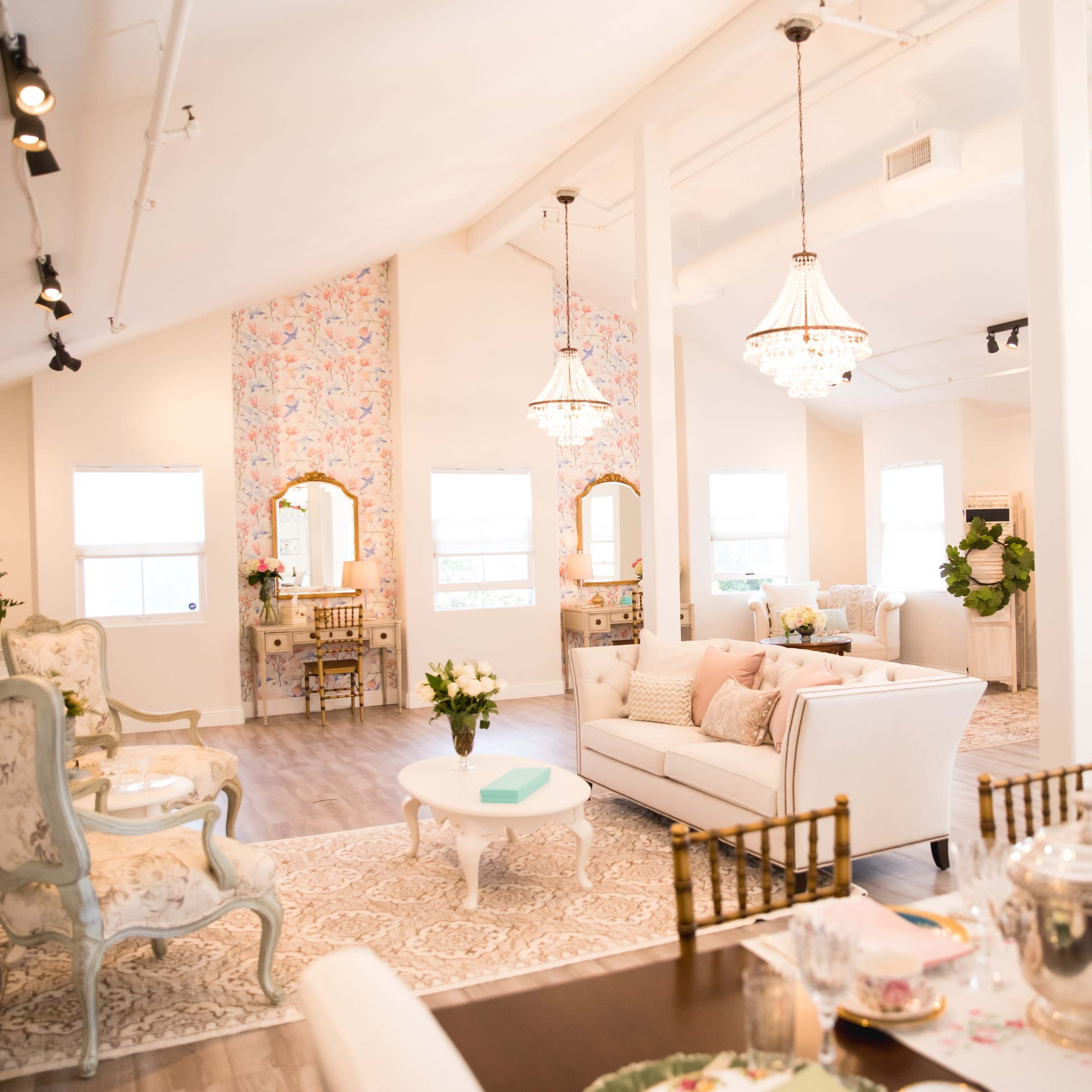 A bright, elegant interior space with vintage-style furniture, floral decor, and a dining area set for tea.