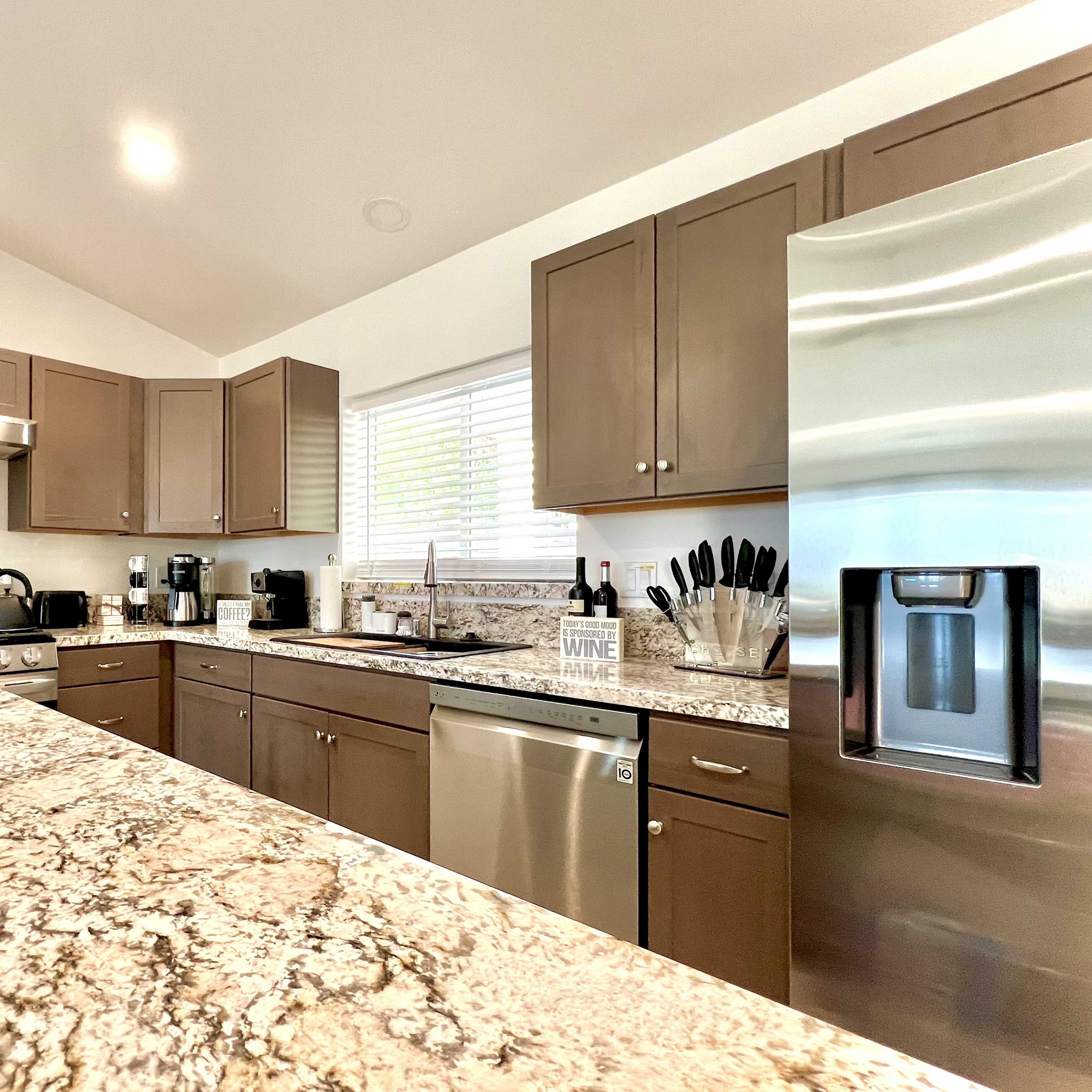 A modern kitchen with dark cabinetry, stainless steel appliances, and a granite countertop featuring a plant and wooden serving tray.