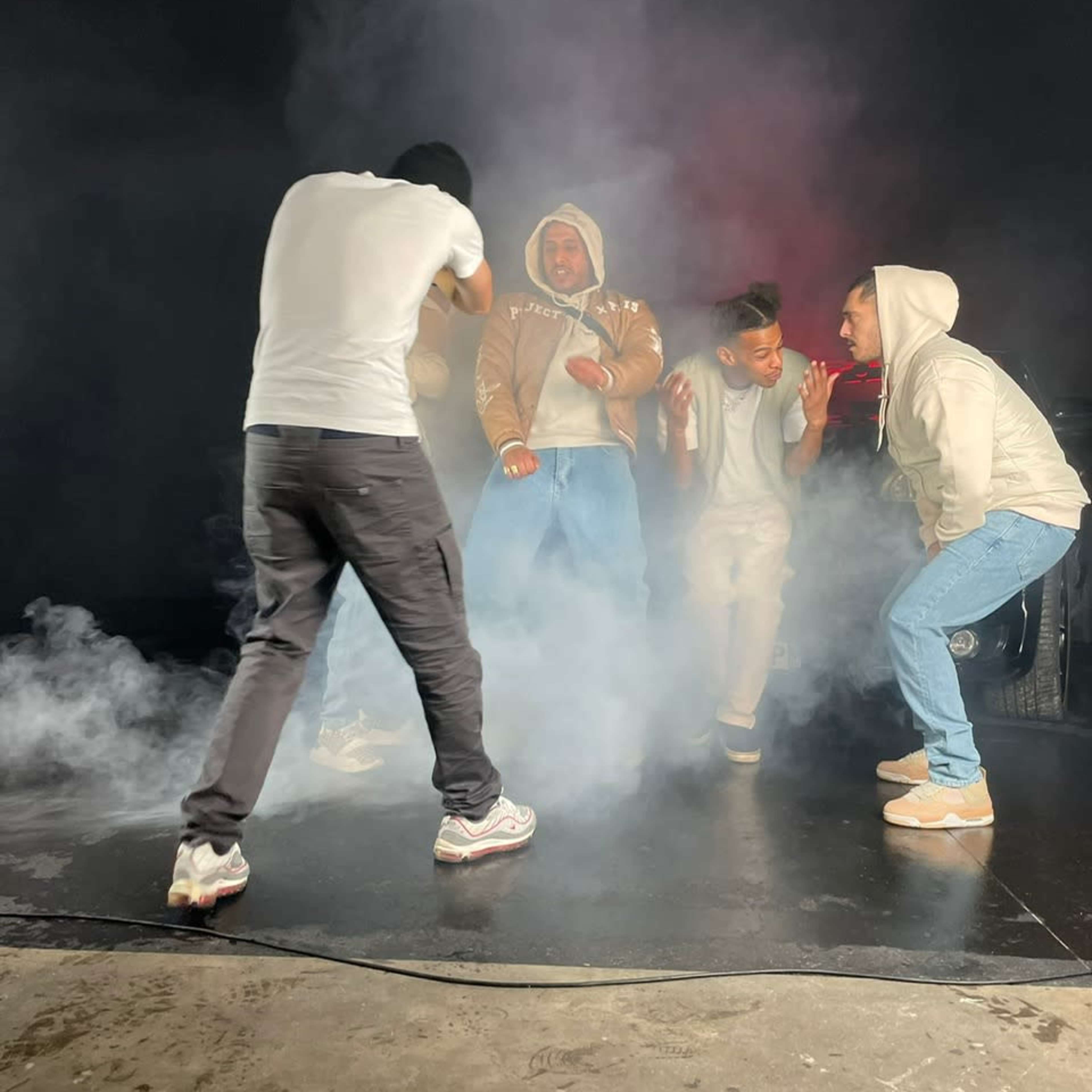 A group of five individuals is posing on a stage surrounded by smoke with one person taking a photo.