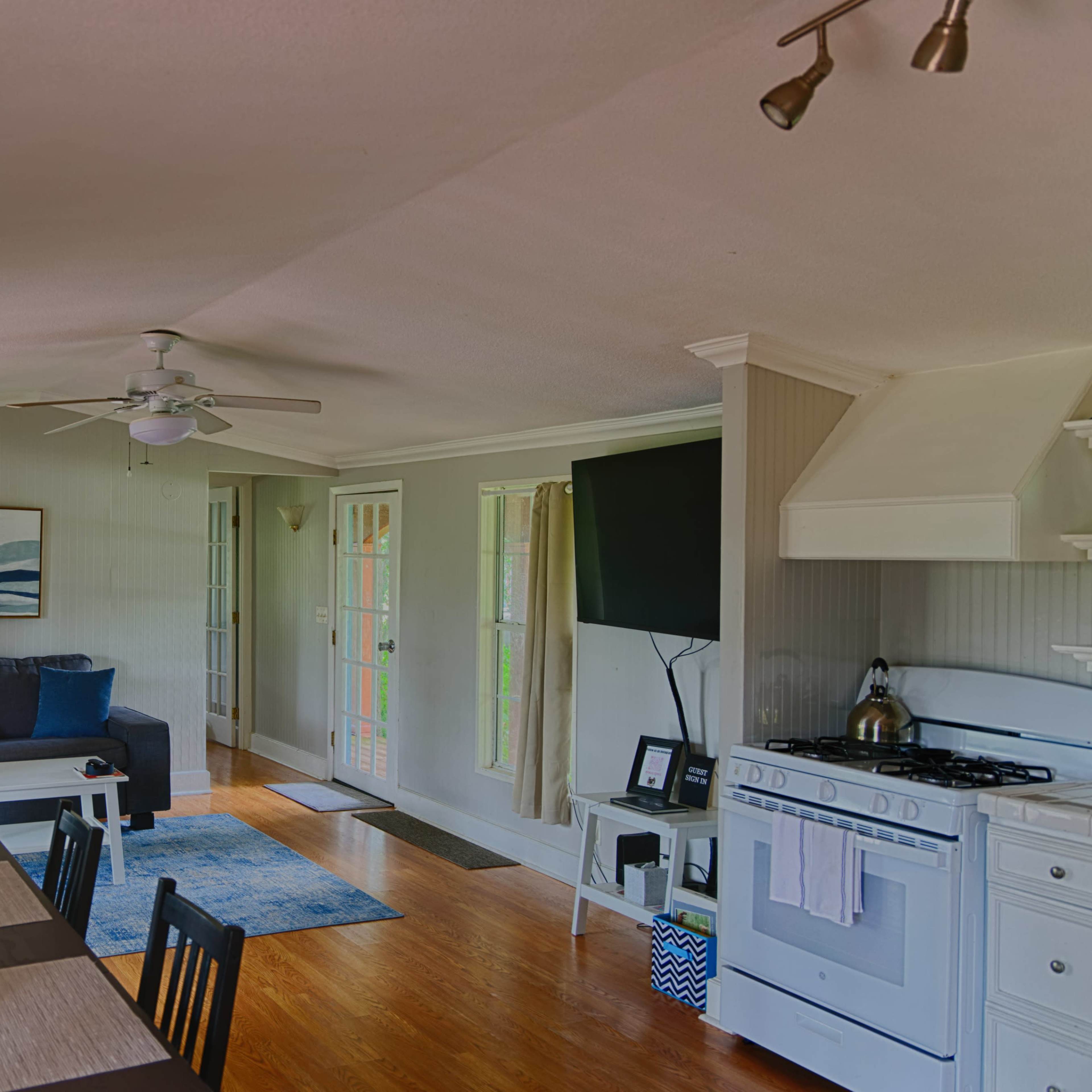 A cozy, open-concept living area with a seating space, dining table, and kitchen, featuring natural light and wooden floors.