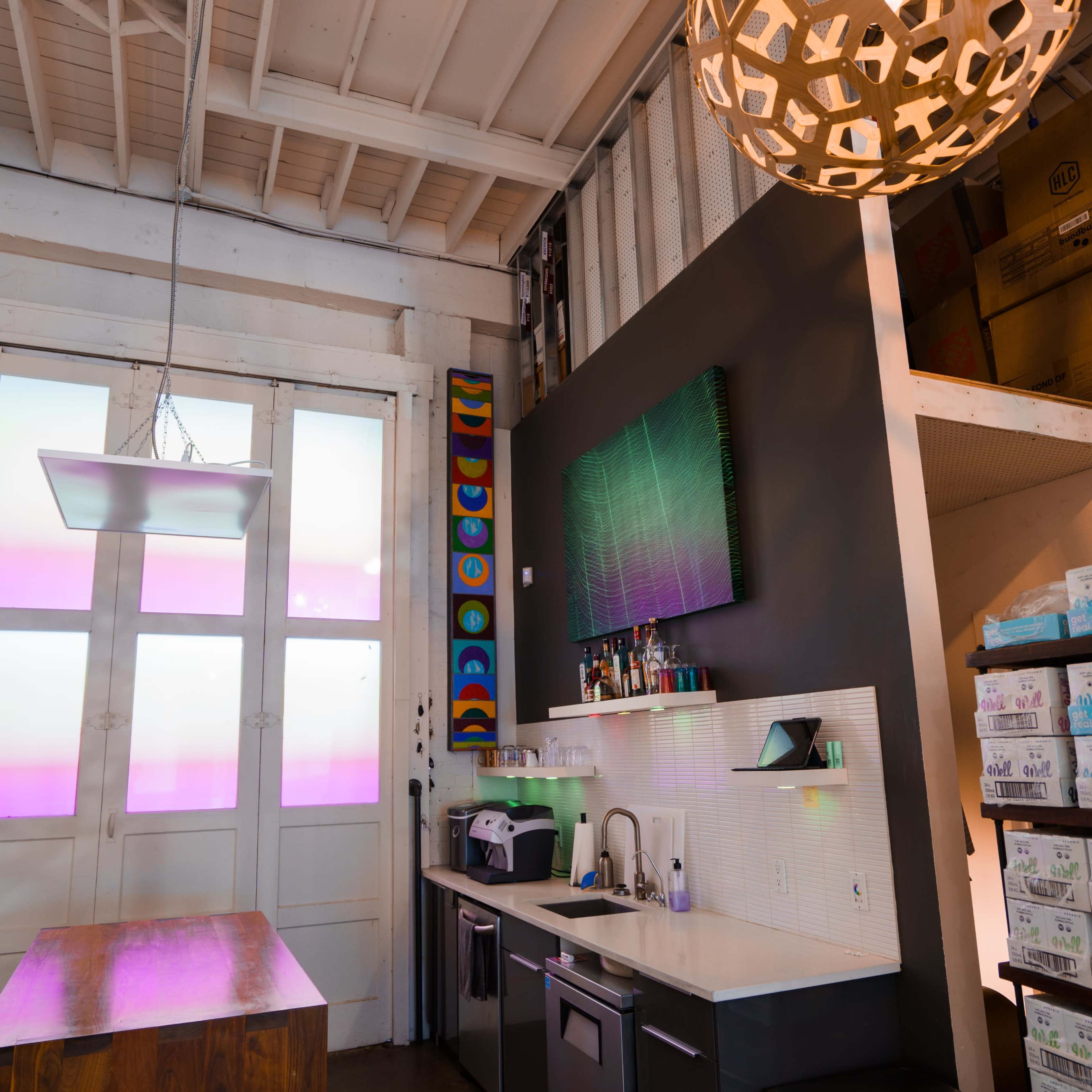 A modern kitchen area with a sleek counter, a wall-mounted TV, and a decorative pendant light hanging from the ceiling.
