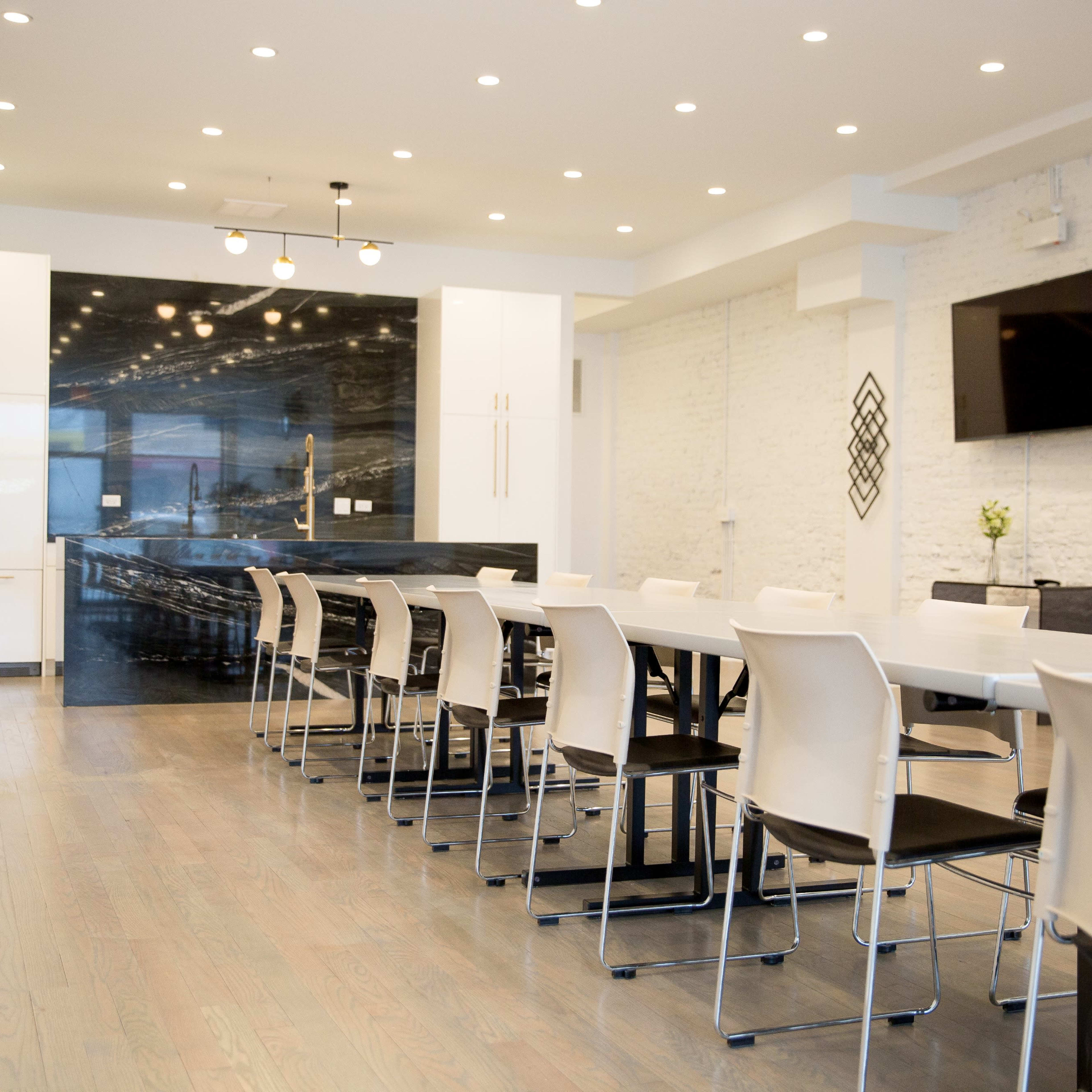 A modern conference room features a long white table surrounded by chairs, with a sleek black wall and a television at the far end.