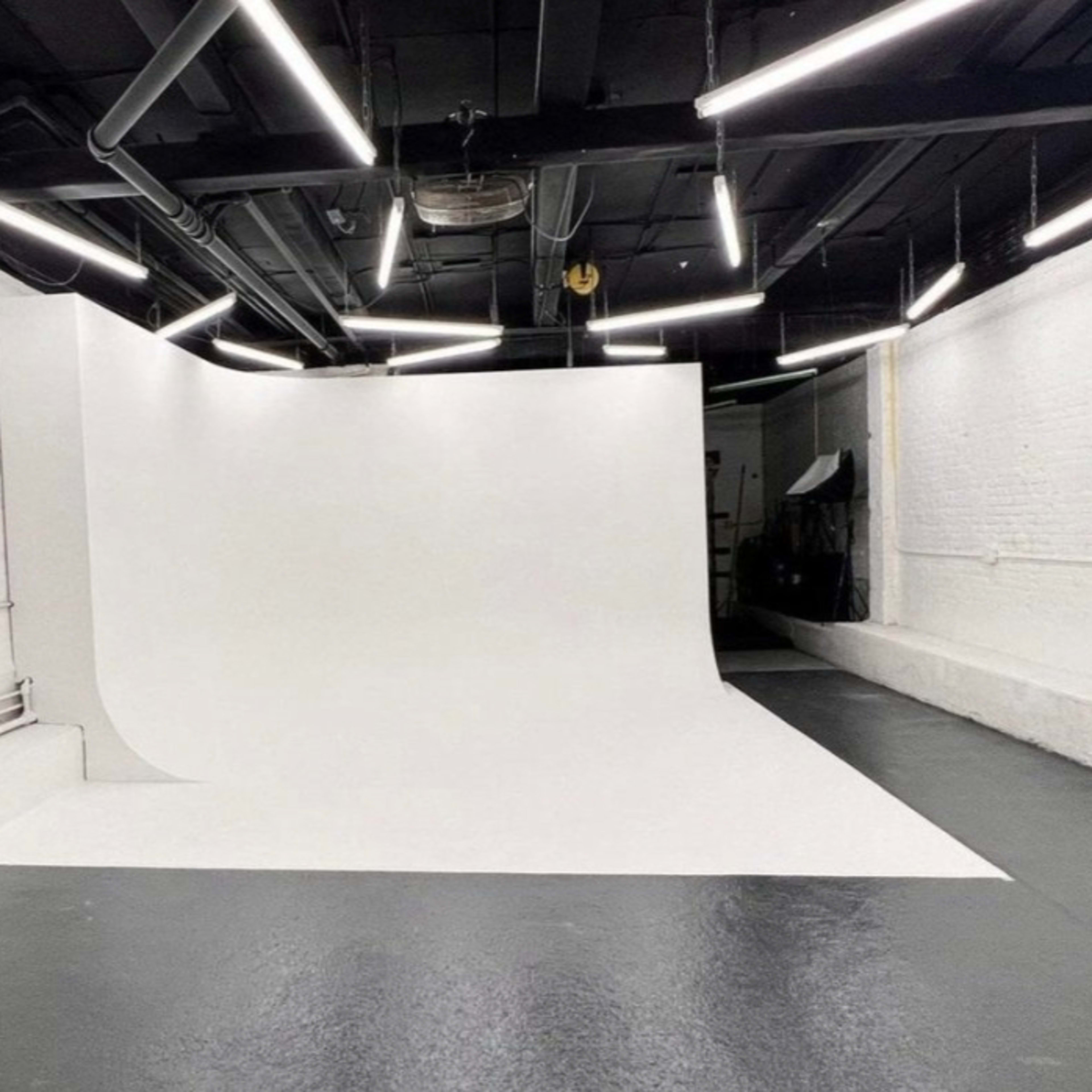 A spacious photography studio with a seamless white backdrop and fluorescent lighting.