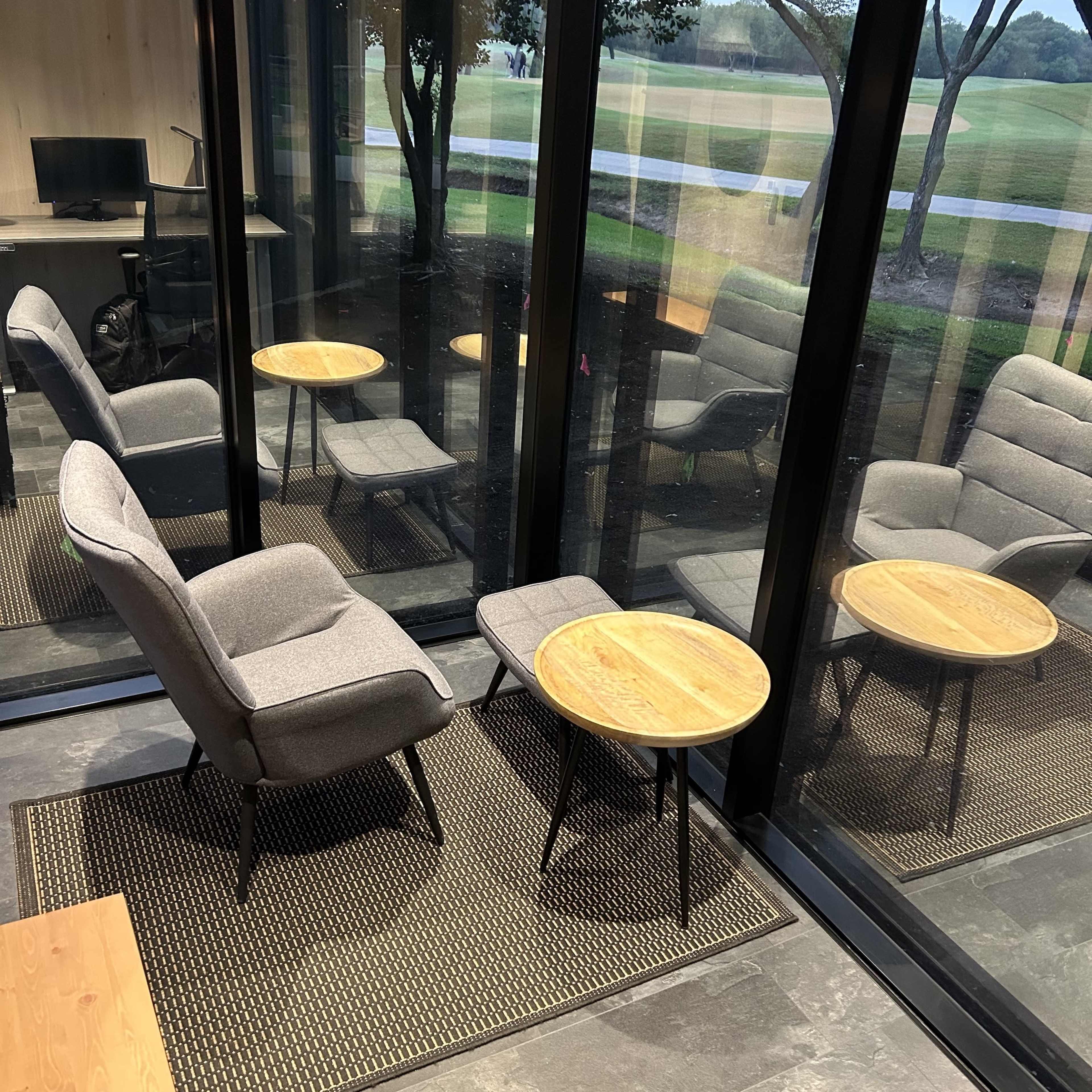 A secluded sitting area with two armchairs and a small round table, enclosed by glass walls and overlooking a green outdoor space.