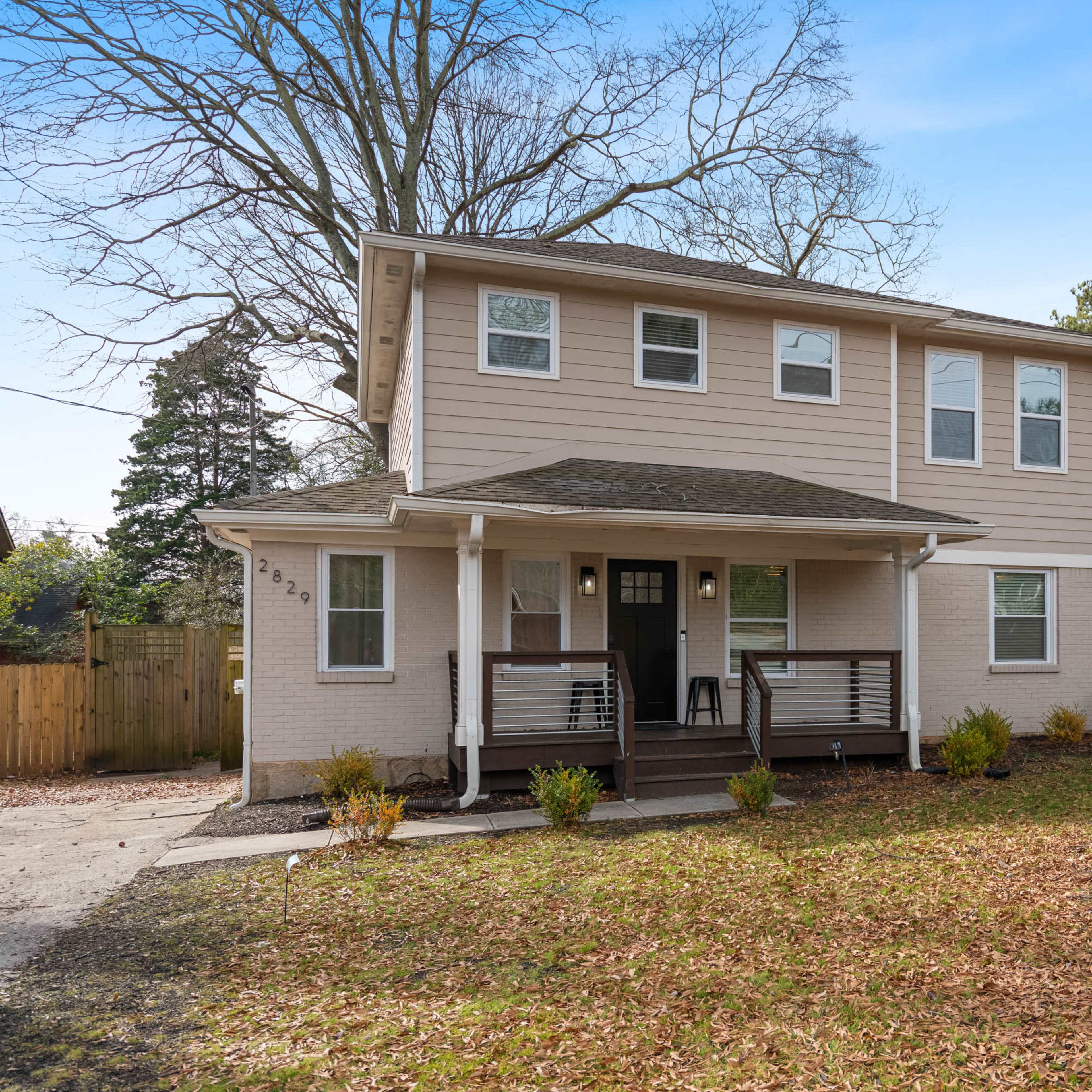 A two-story house with a covered front porch sits on a landscaped lot surrounded by trees.