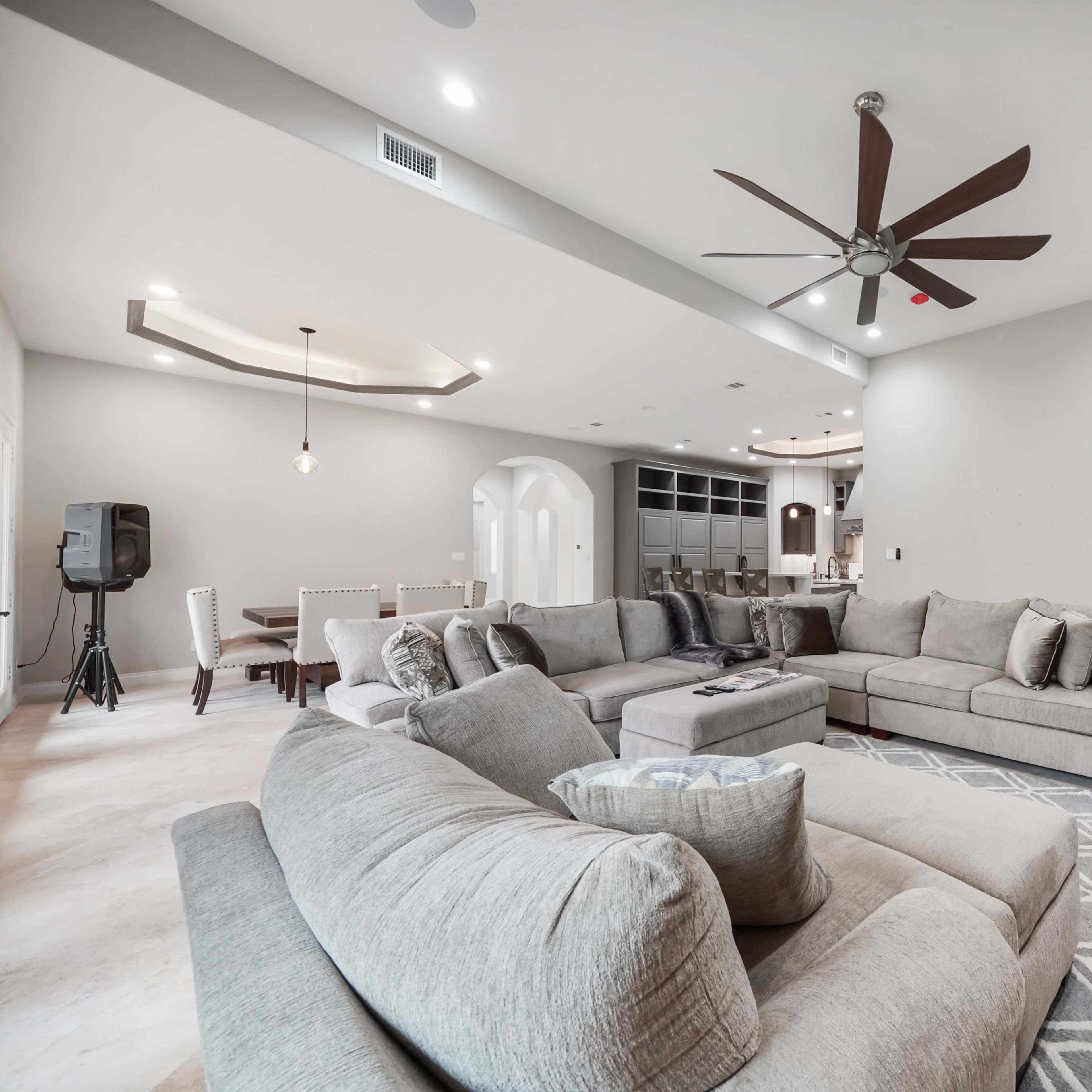 A spacious living room with a gray sectional sofa, a ceiling fan, and a view of a dining area in the background.