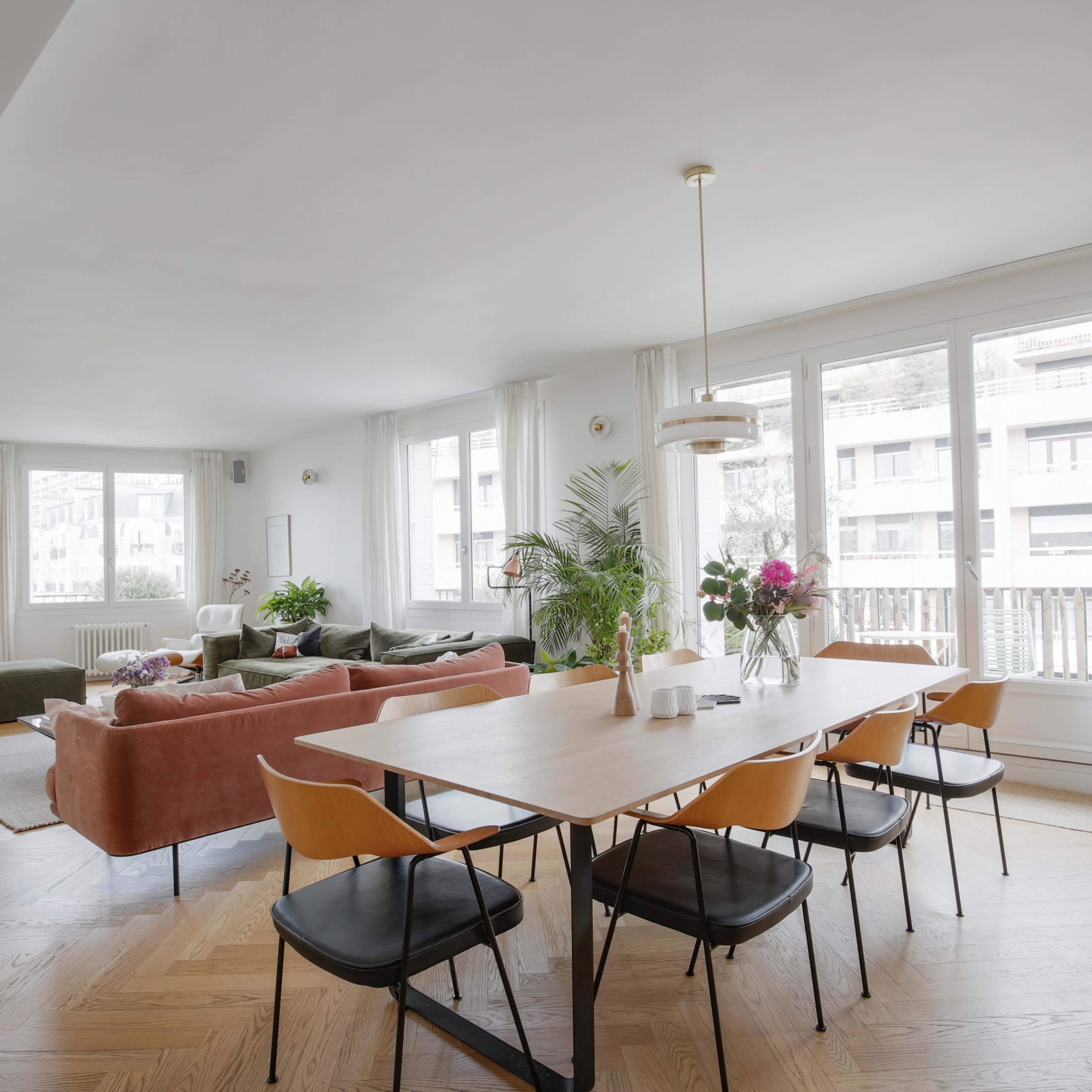 A modern, open-concept living and dining area with large windows, a wooden dining table, and a mix of green and orange seating.