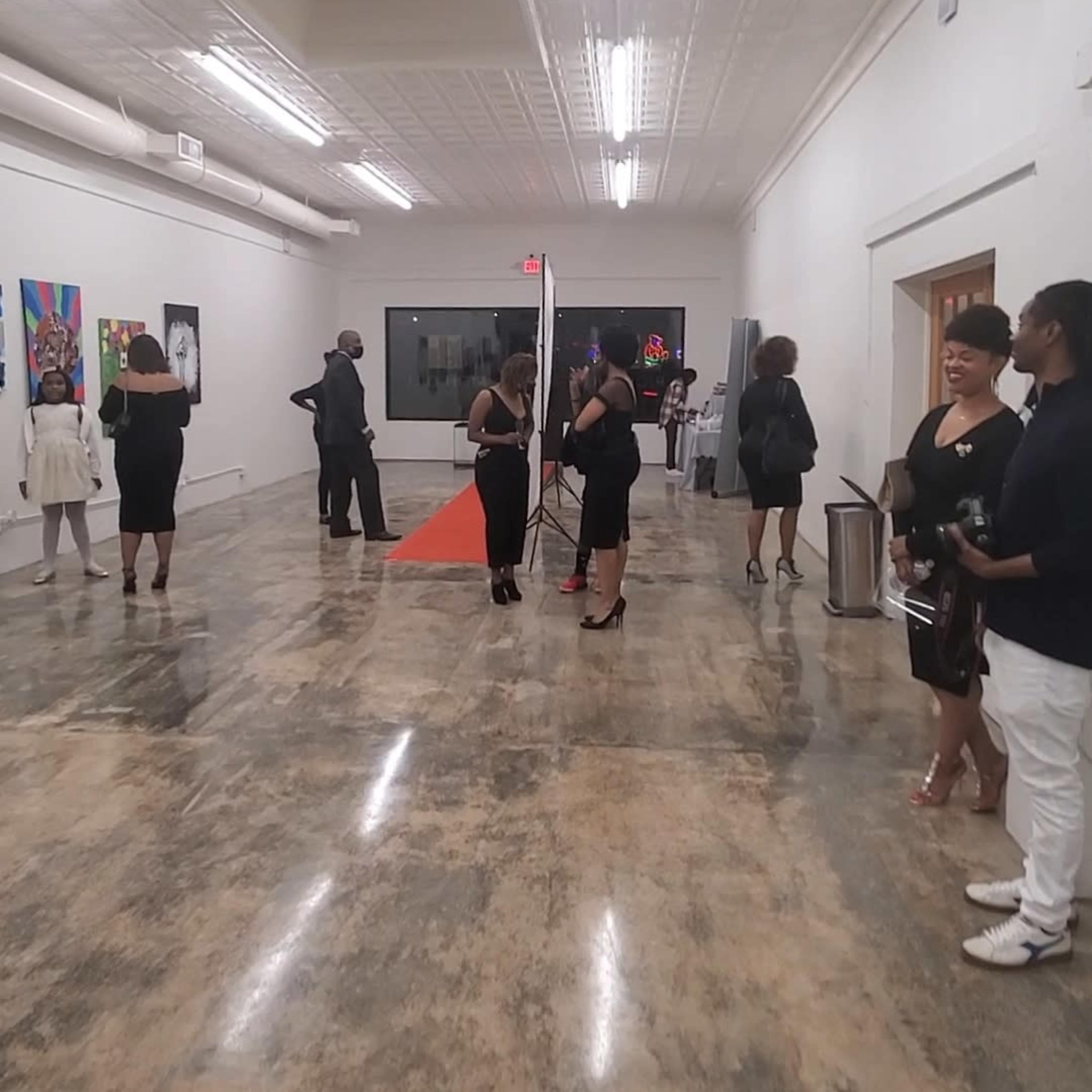 A group of people in formal attire gathered in a spacious gallery with colorful artwork displayed on the walls.