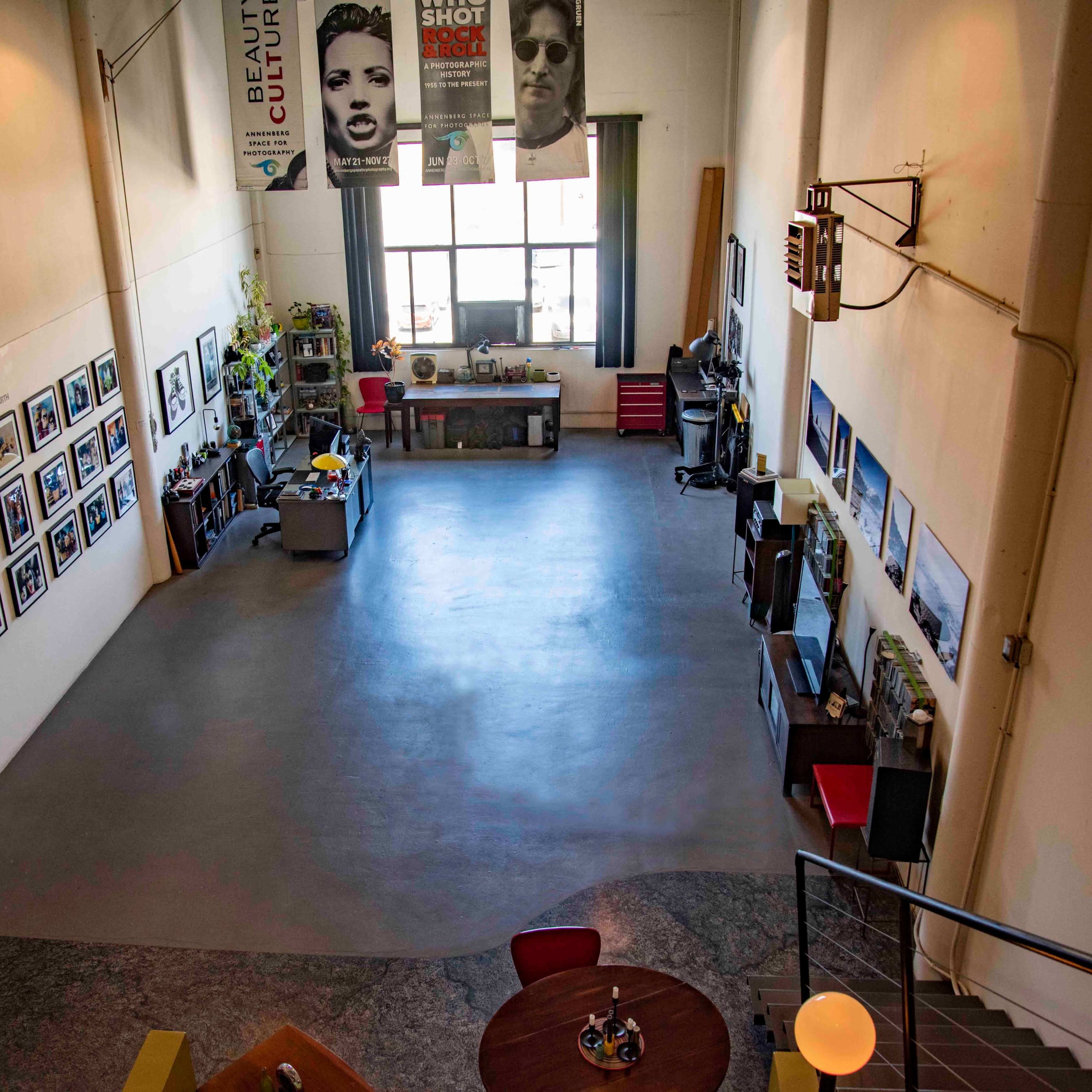 A spacious art studio with a concrete floor, walls adorned with framed photographs, and various workstations along the sides.