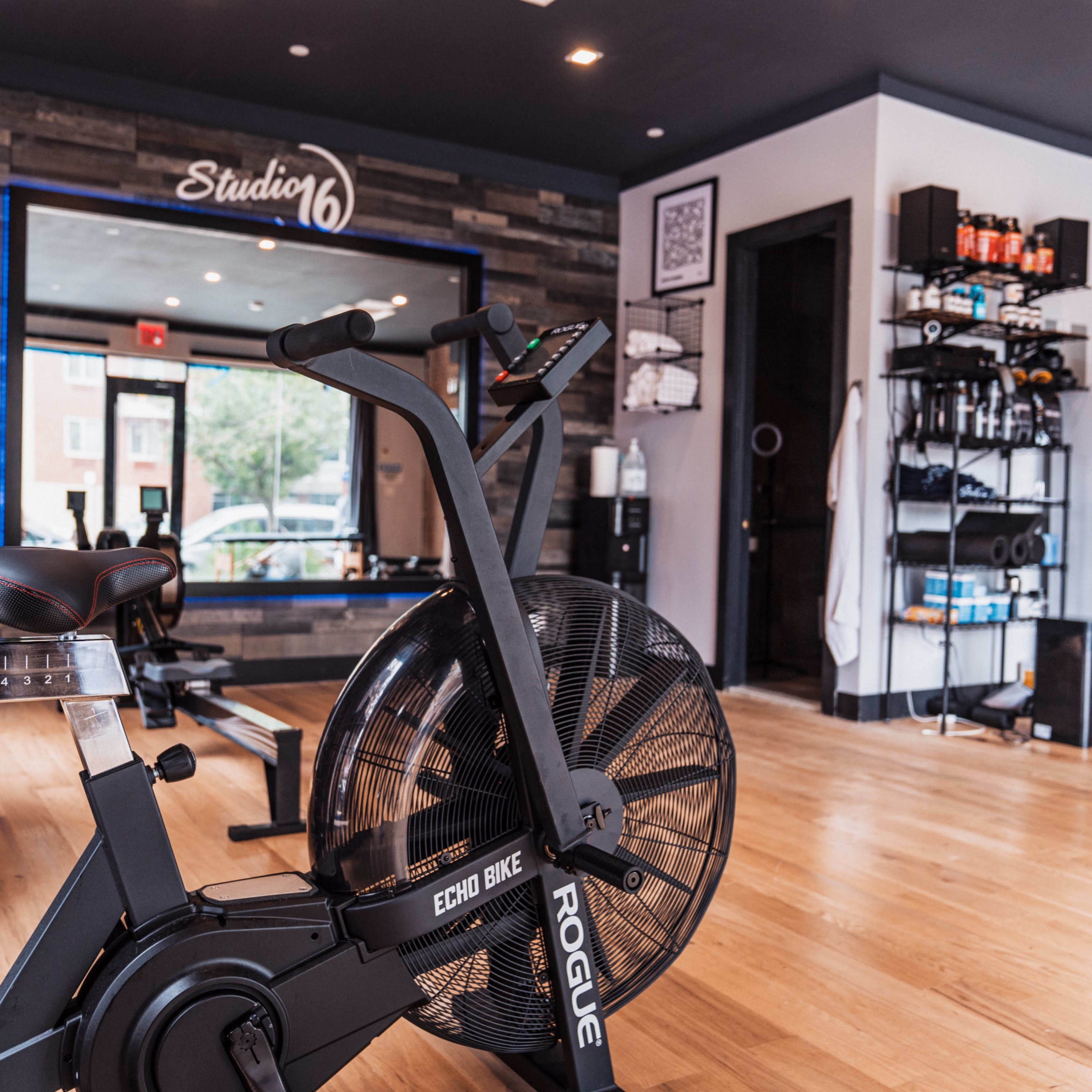 A fitness studio featuring an Echo Bike in the foreground, with weights and storage shelves visible in the background.