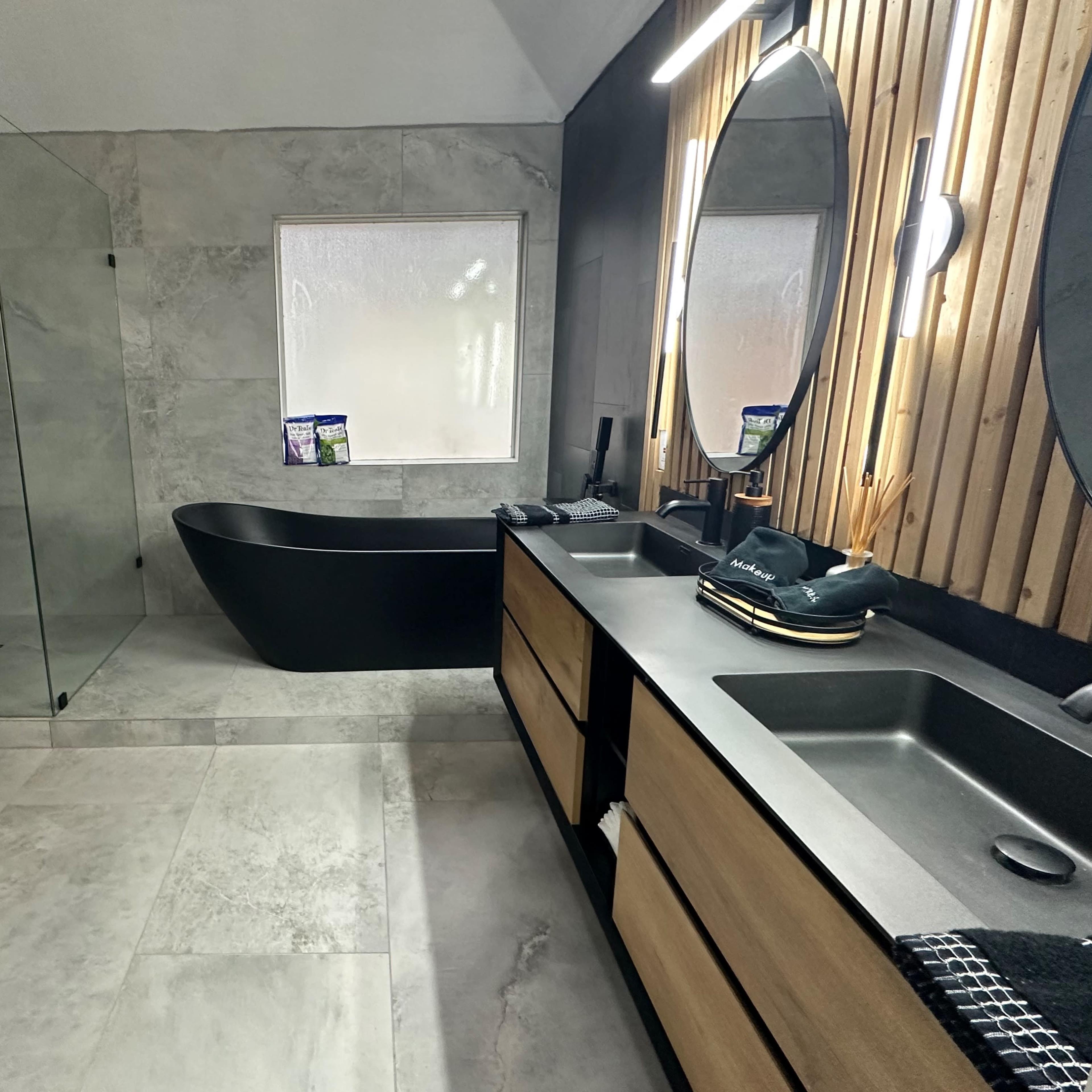 A modern bathroom featuring a glass shower enclosure, a freestanding black bathtub, dual mirrors, and a wooden vanity with sink.