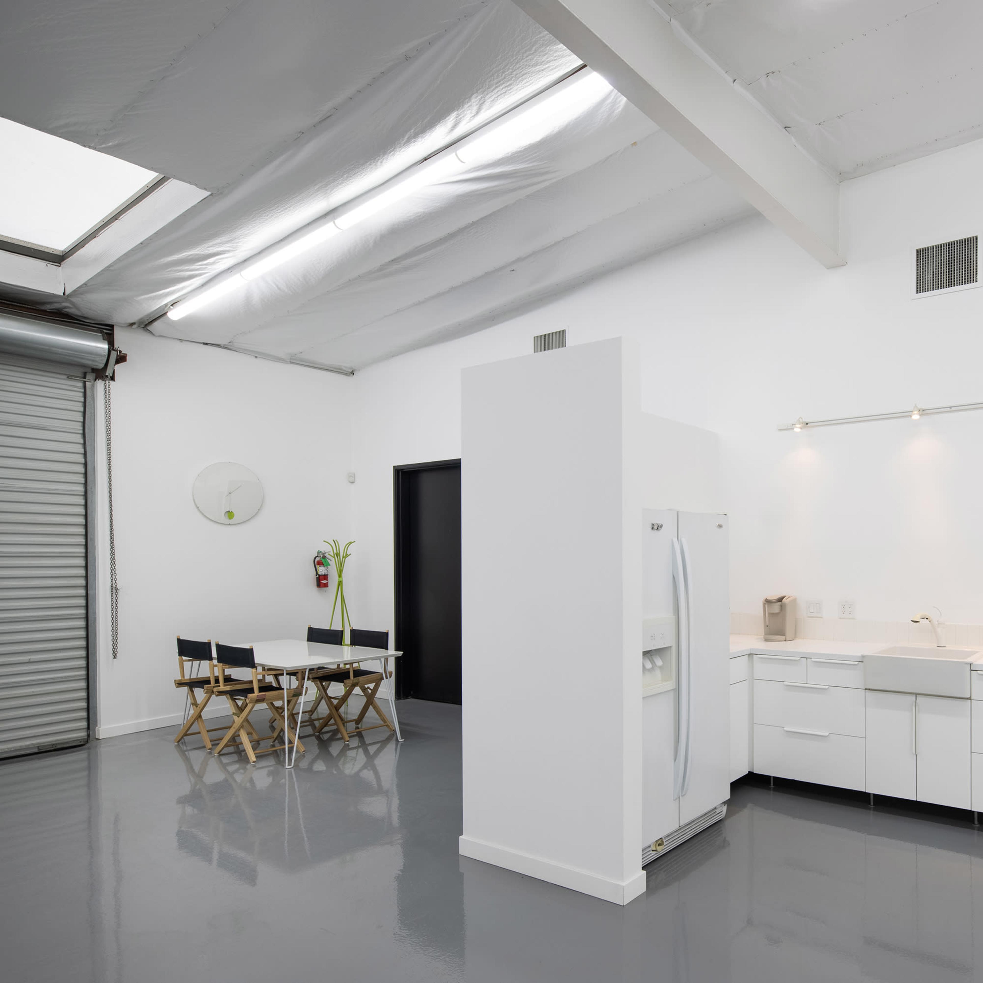 A minimalist kitchen area with white cabinetry, a stove, a refrigerator, and a dining table with two chairs.