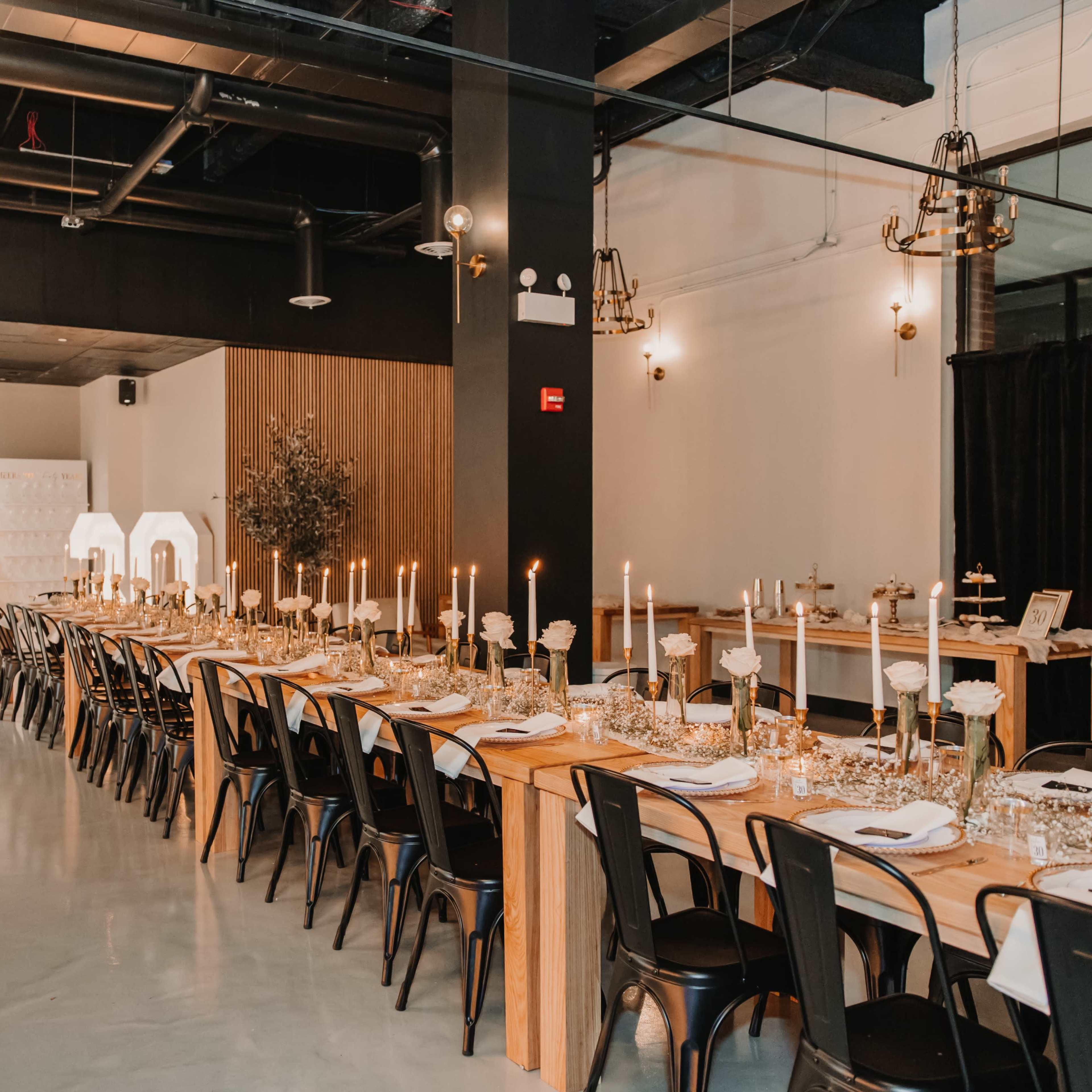A long dining table is adorned with candles and flowers in a modern event space featuring decorative elements and elegant lighting.