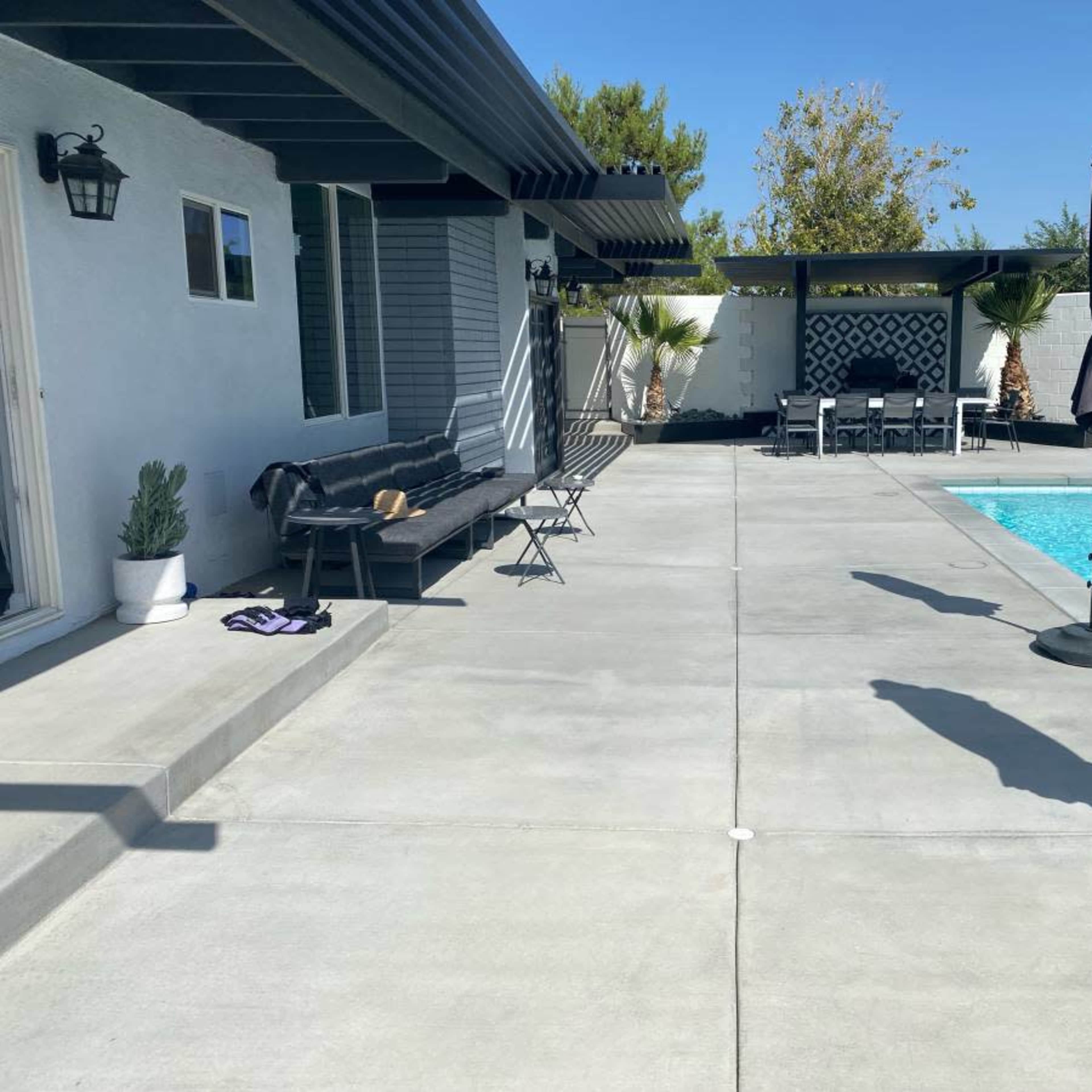 A modern backyard featuring a swimming pool, lounge chairs, and patio umbrellas against a clear blue sky.