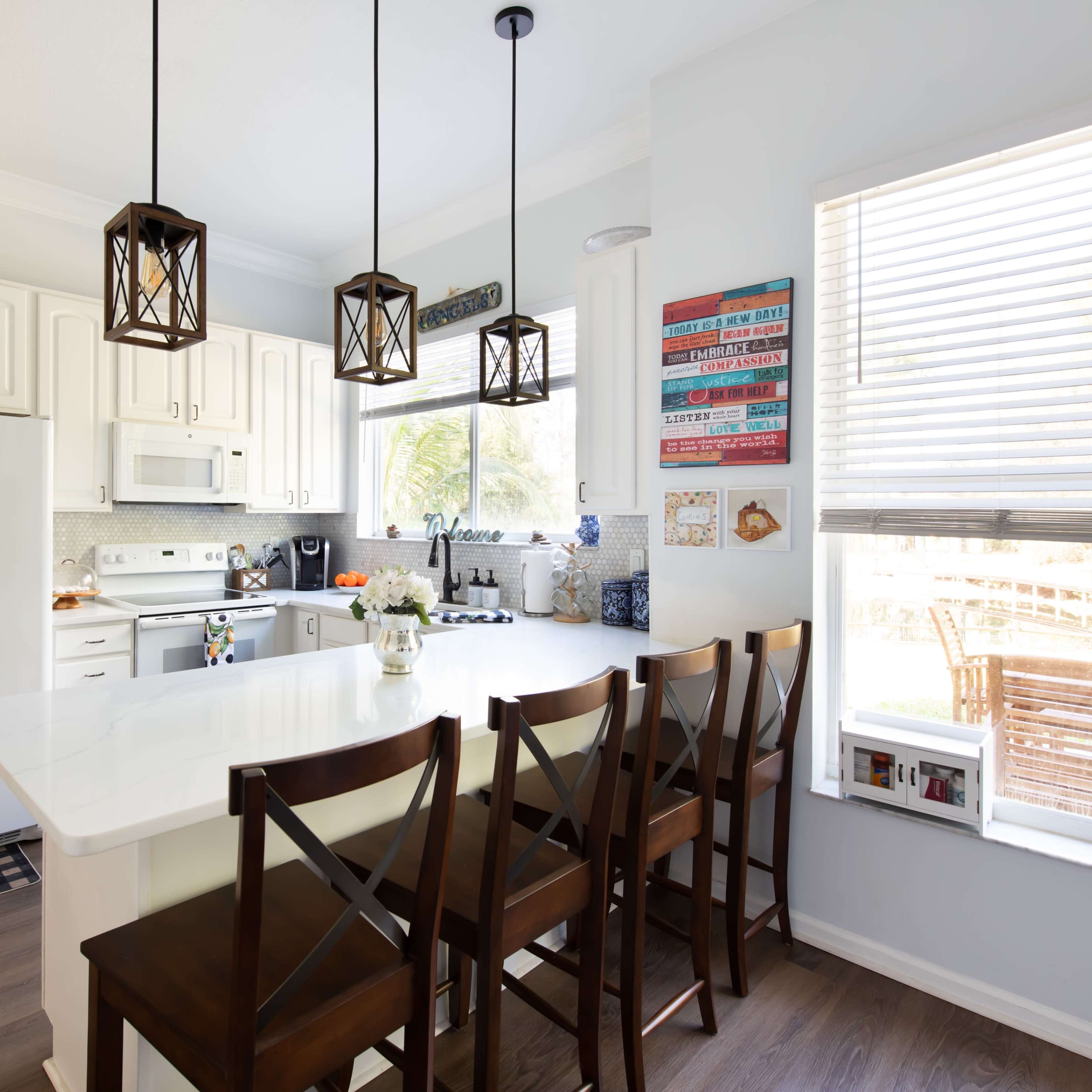 A modern kitchen features white cabinetry, a large island with bar stools, and pendant lighting over the counter.