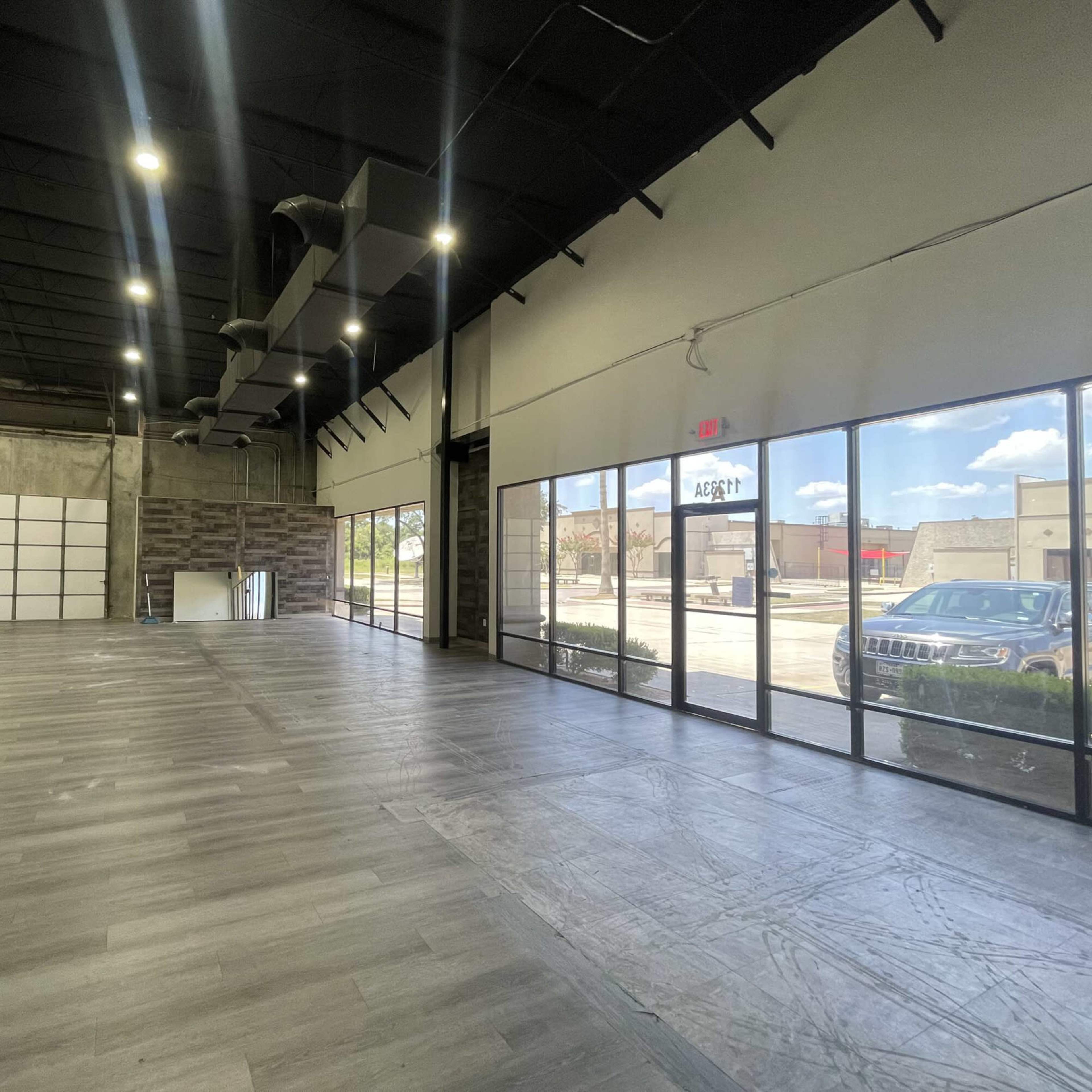 A spacious, empty commercial interior with large windows and a polished wooden floor.