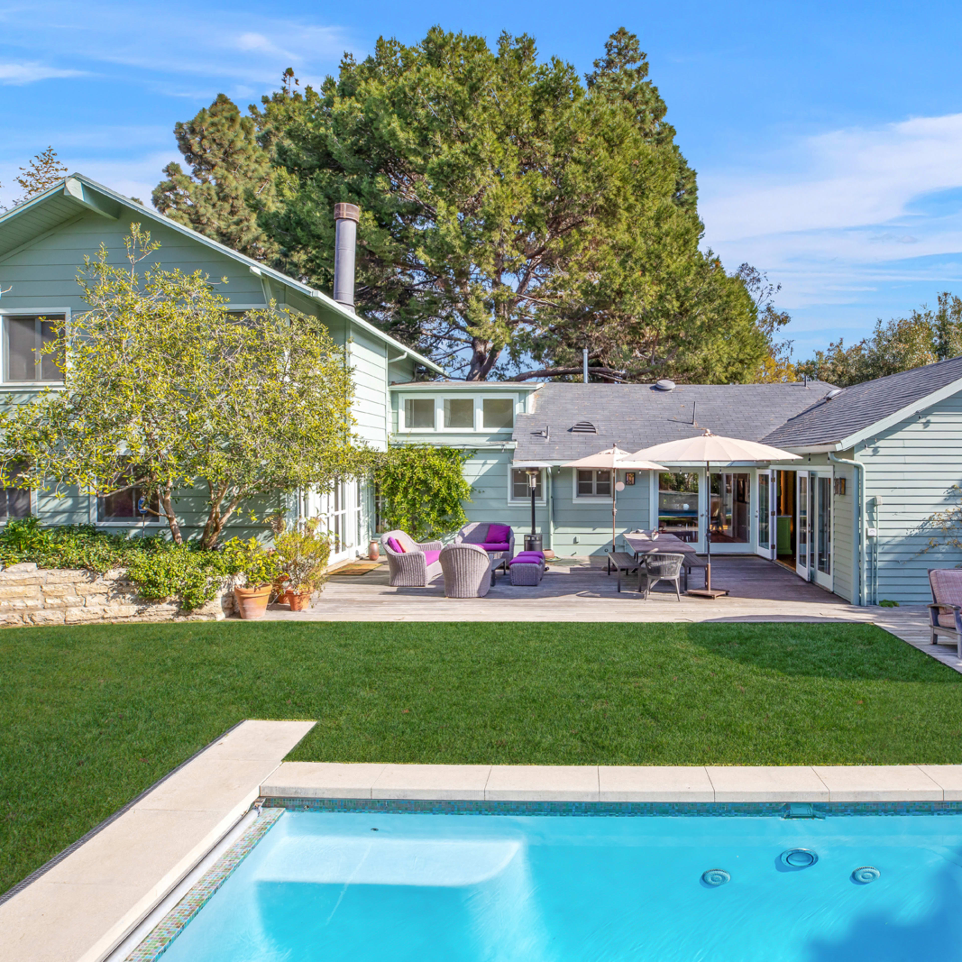 A modern house with light blue siding, a well-maintained lawn, and a swimming pool in the foreground.