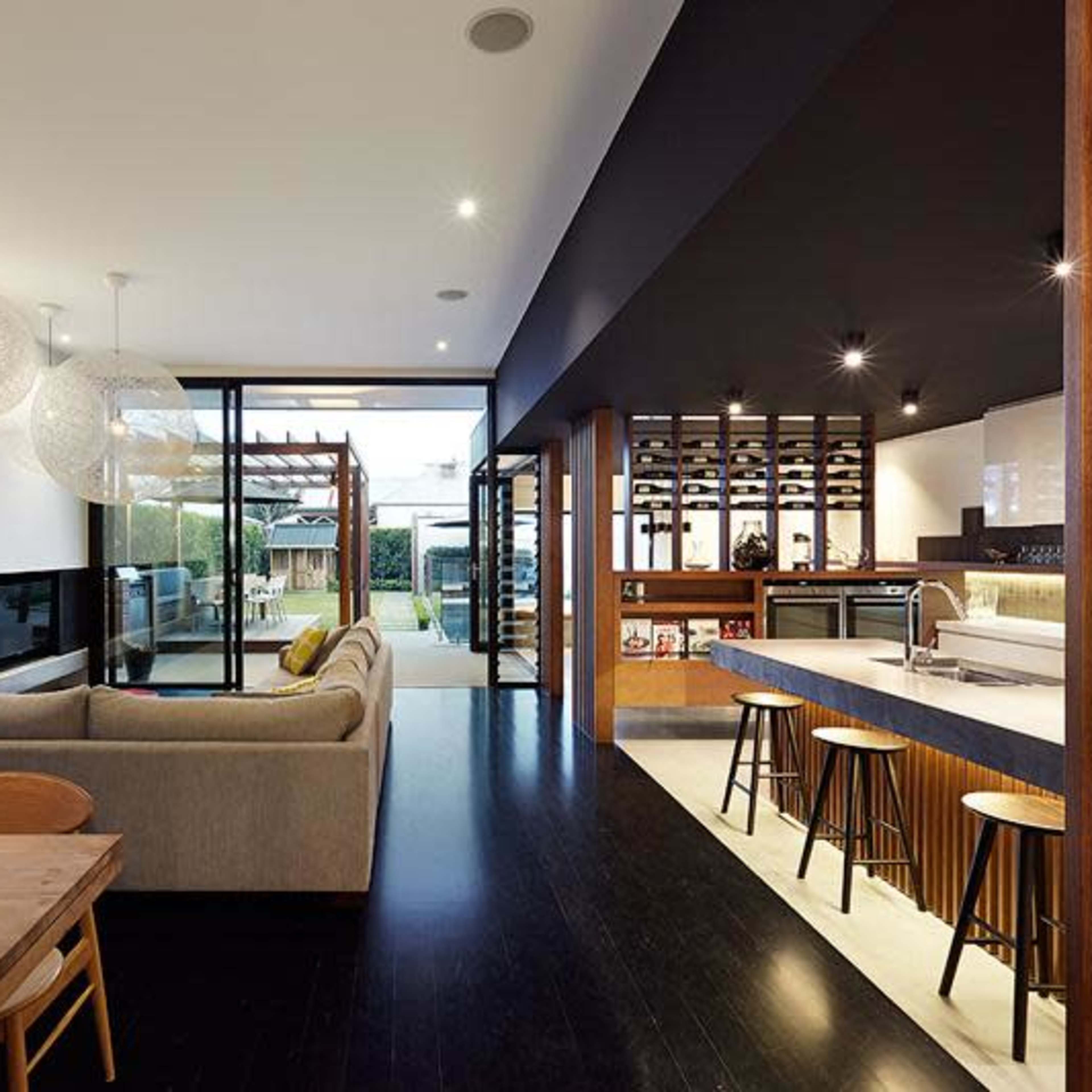 A modern open-concept living area with a sofa, dining table, and kitchen, showcasing large glass doors that lead to an outdoor space.