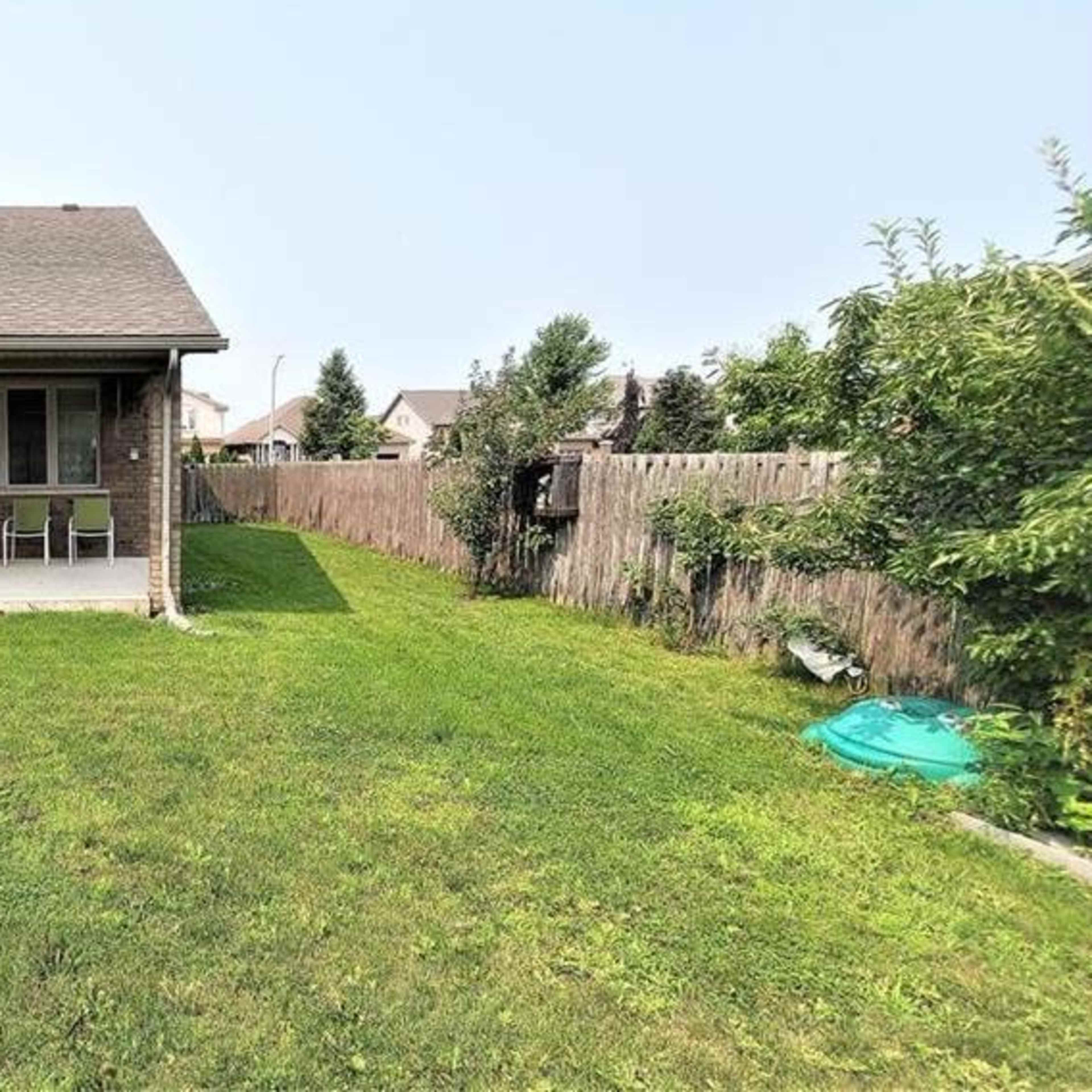 A backyard features a patio area with two chairs, a grill, and a neatly maintained lawn bordered by a wooden fence.