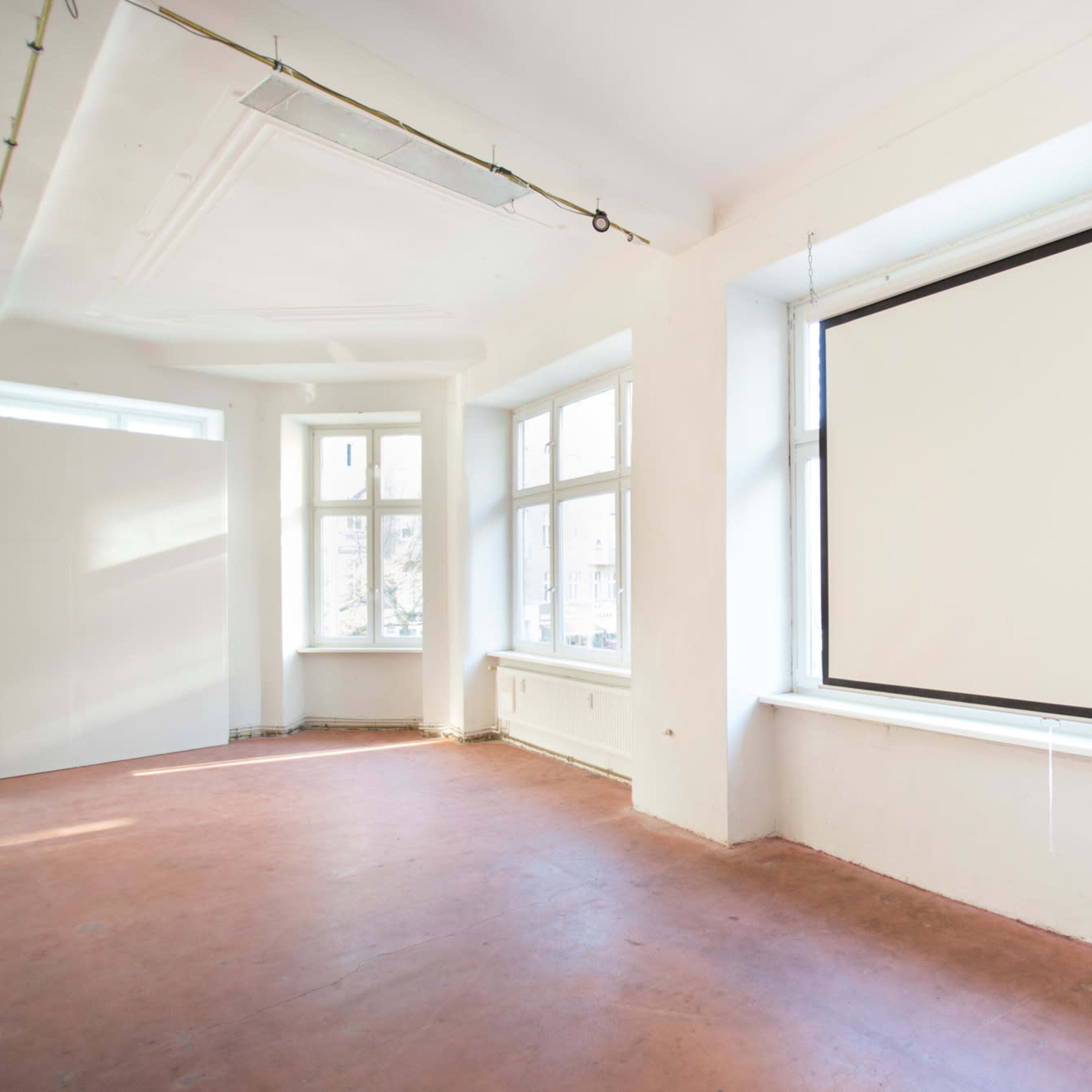A bright, empty room with large windows and a retractable projection screen mounted on a wall.