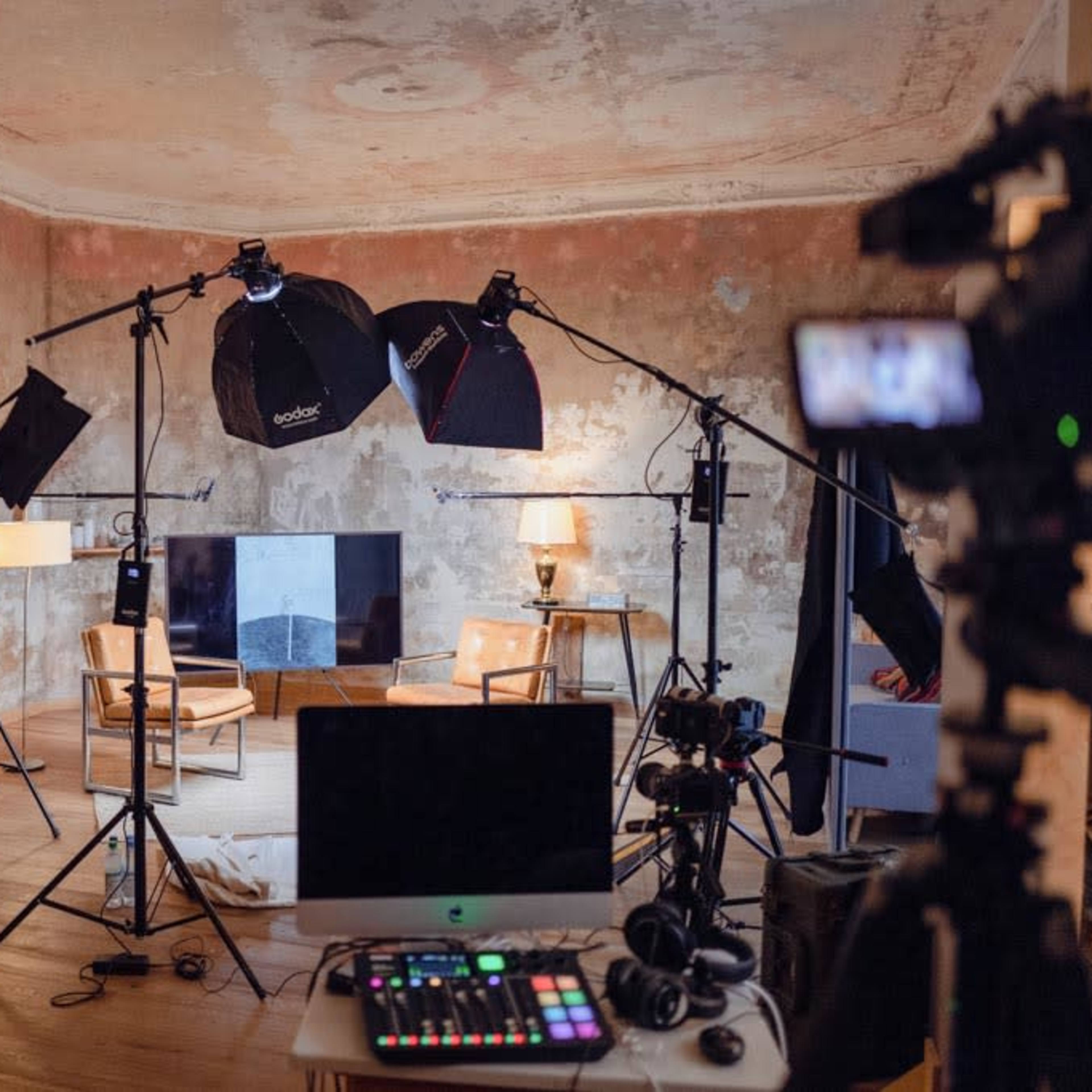 A film or photography studio setup with multiple cameras, lights, and a computer in a room with weathered walls and wooden flooring.
