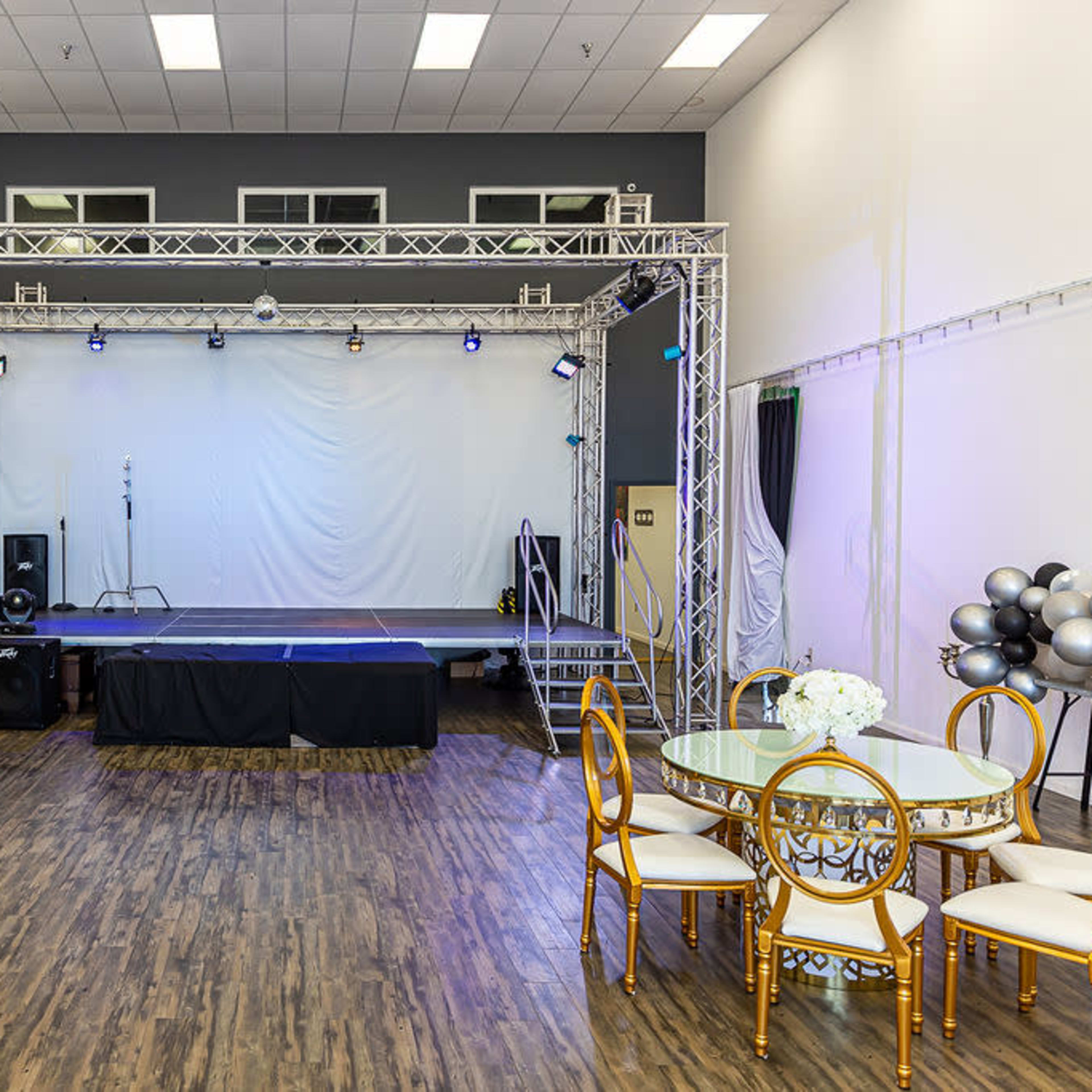A spacious event venue with a stage at one end and round dining tables set up facing the stage.