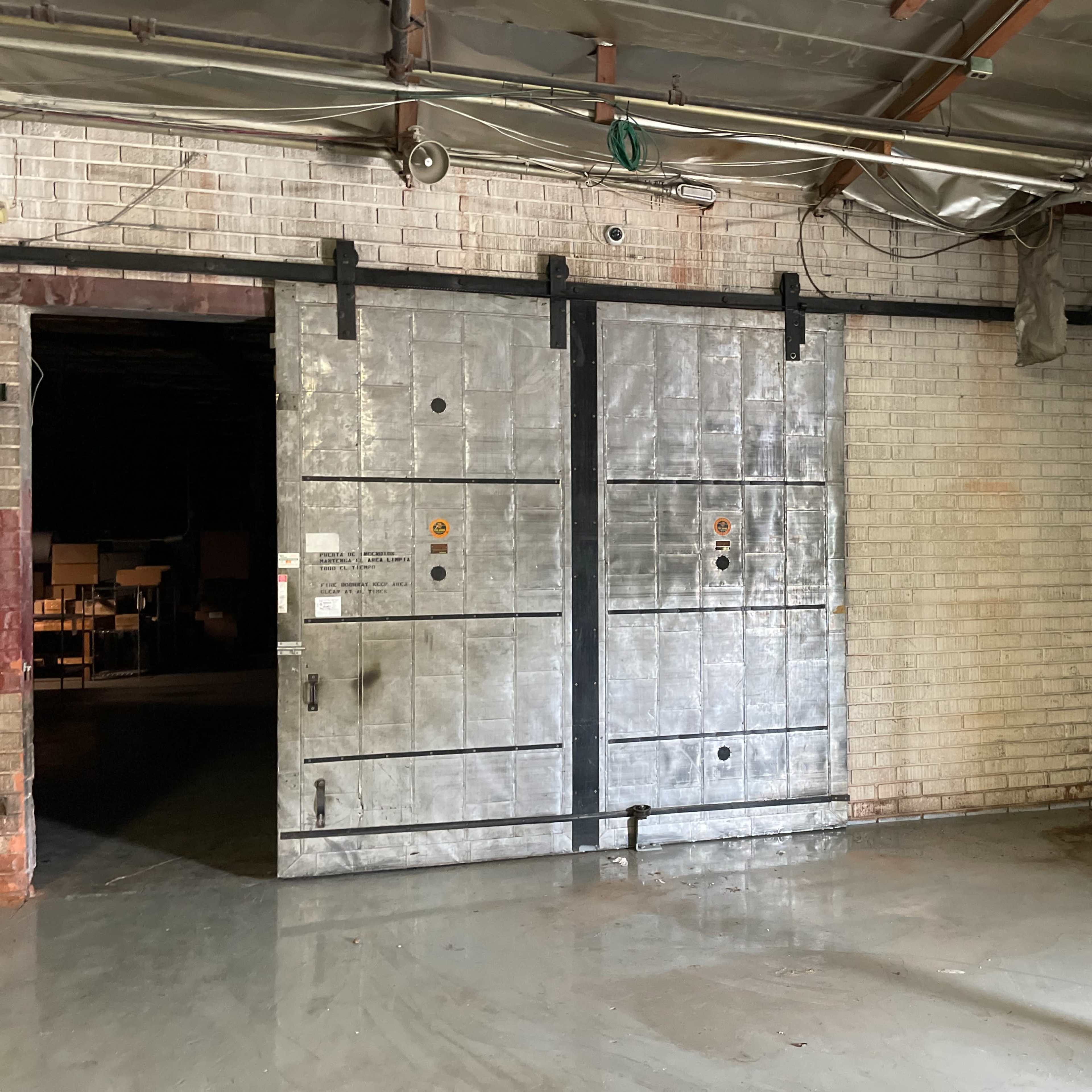 A large, industrial metal door within a concrete-walled warehouse space.