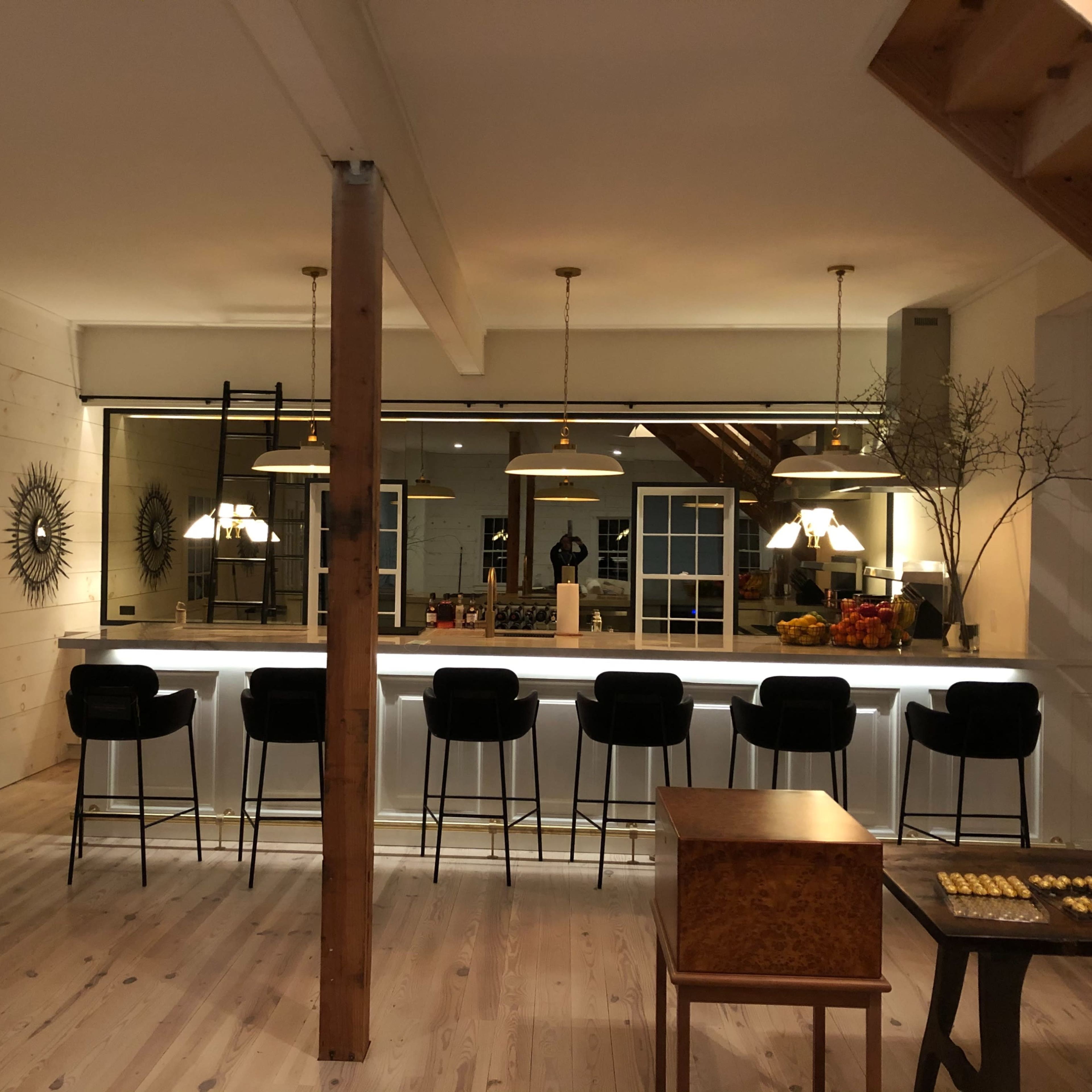 A modern, well-lit kitchen with a large bar counter, high stools, and a mirror backing, along with decorative elements like wall mirrors and fruit on display.