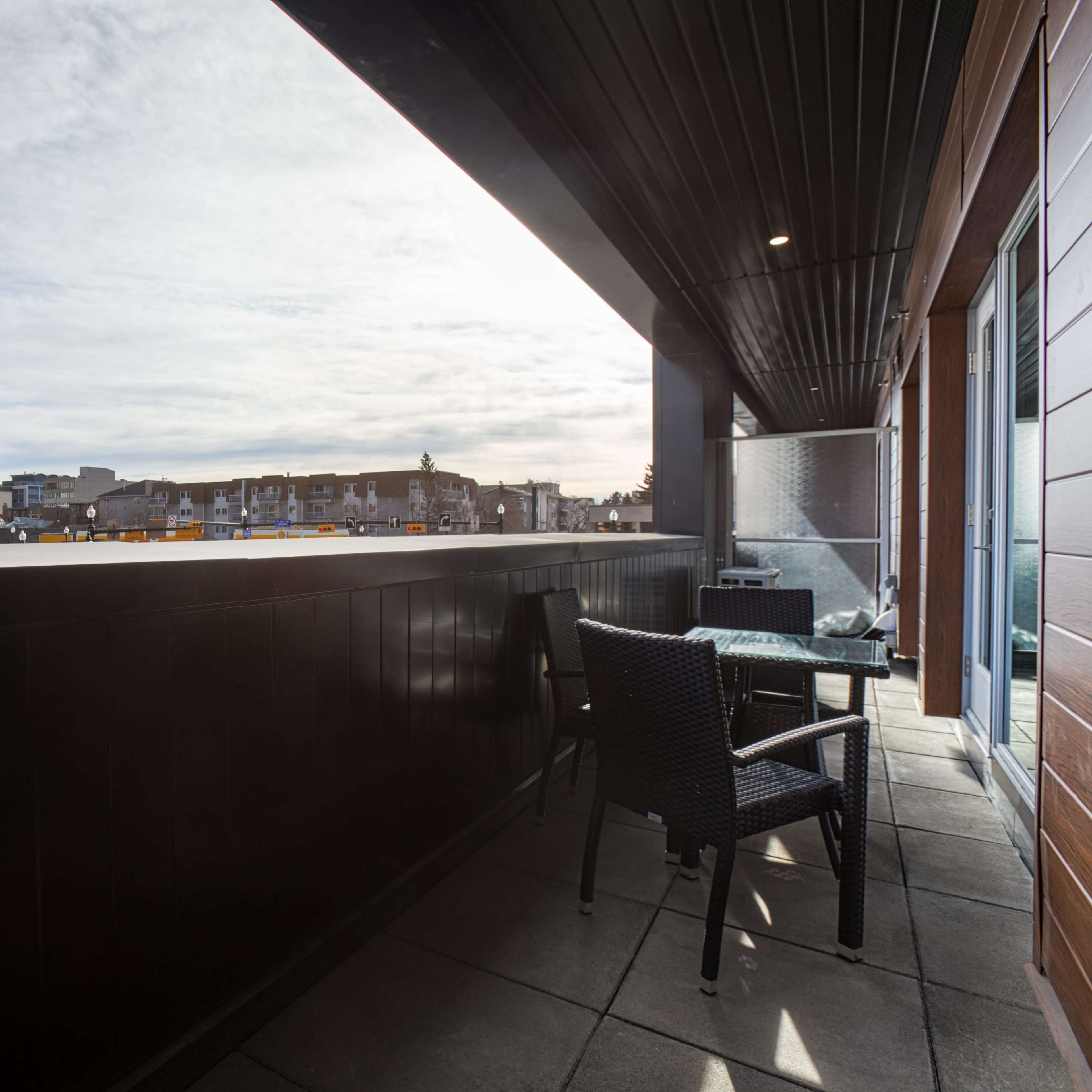 A balcony with a table and chair overlooking a cityscape under a partly cloudy sky.