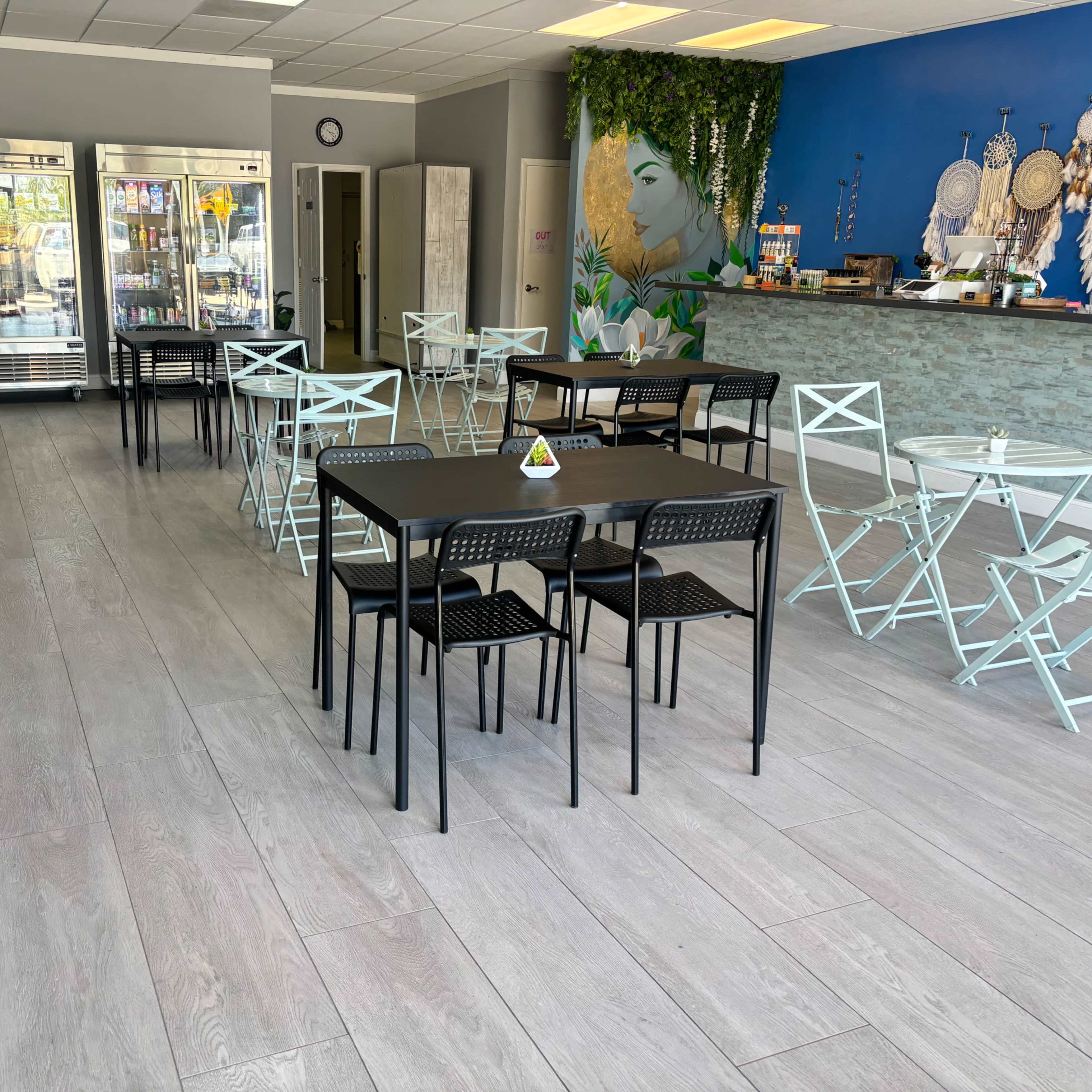 A bright, modern cafe interior with black tables and chairs arranged neatly on light-colored flooring, against a blue wall adorned with decorative items.