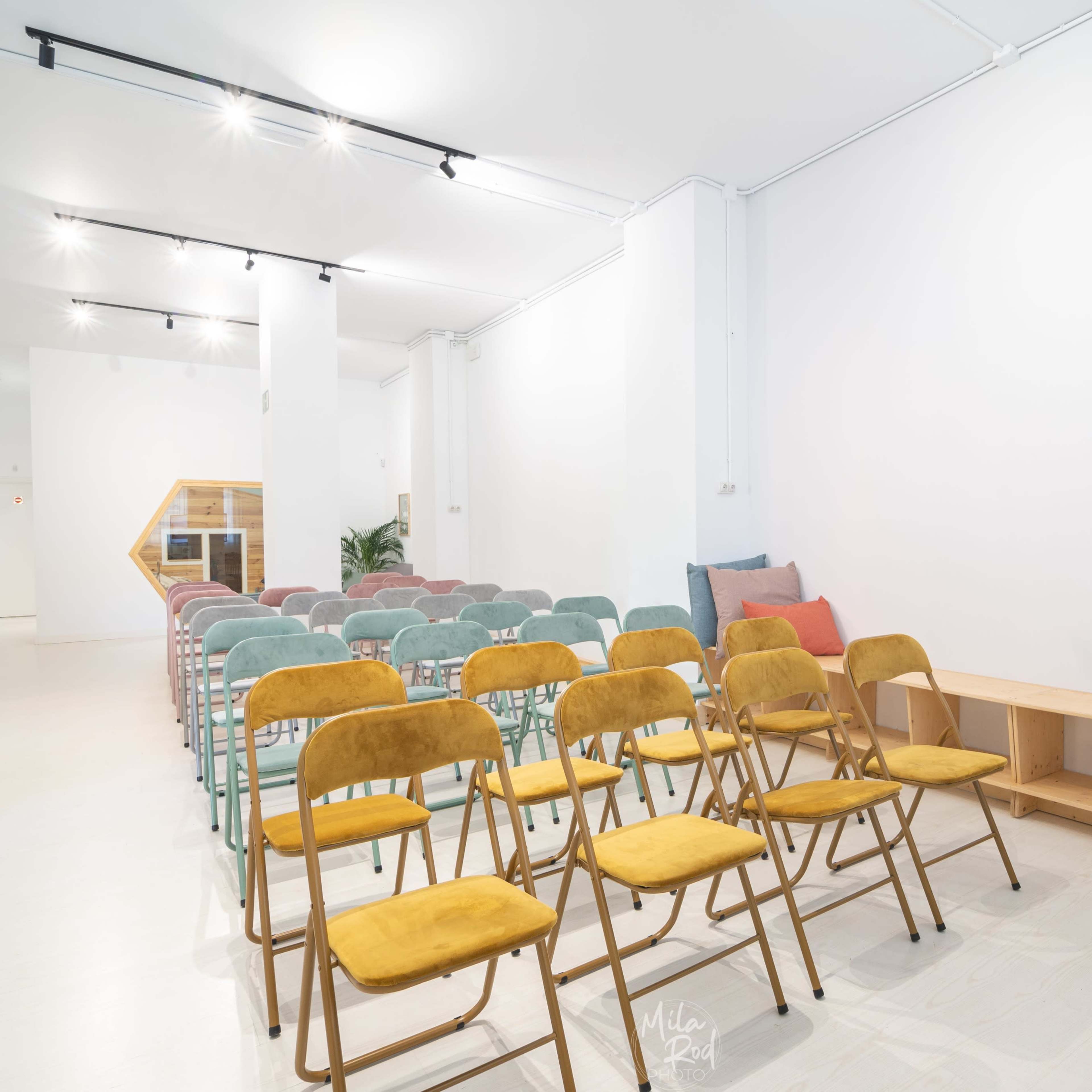 A spacious room set up for an event with rows of colored chairs and a wooden bench.