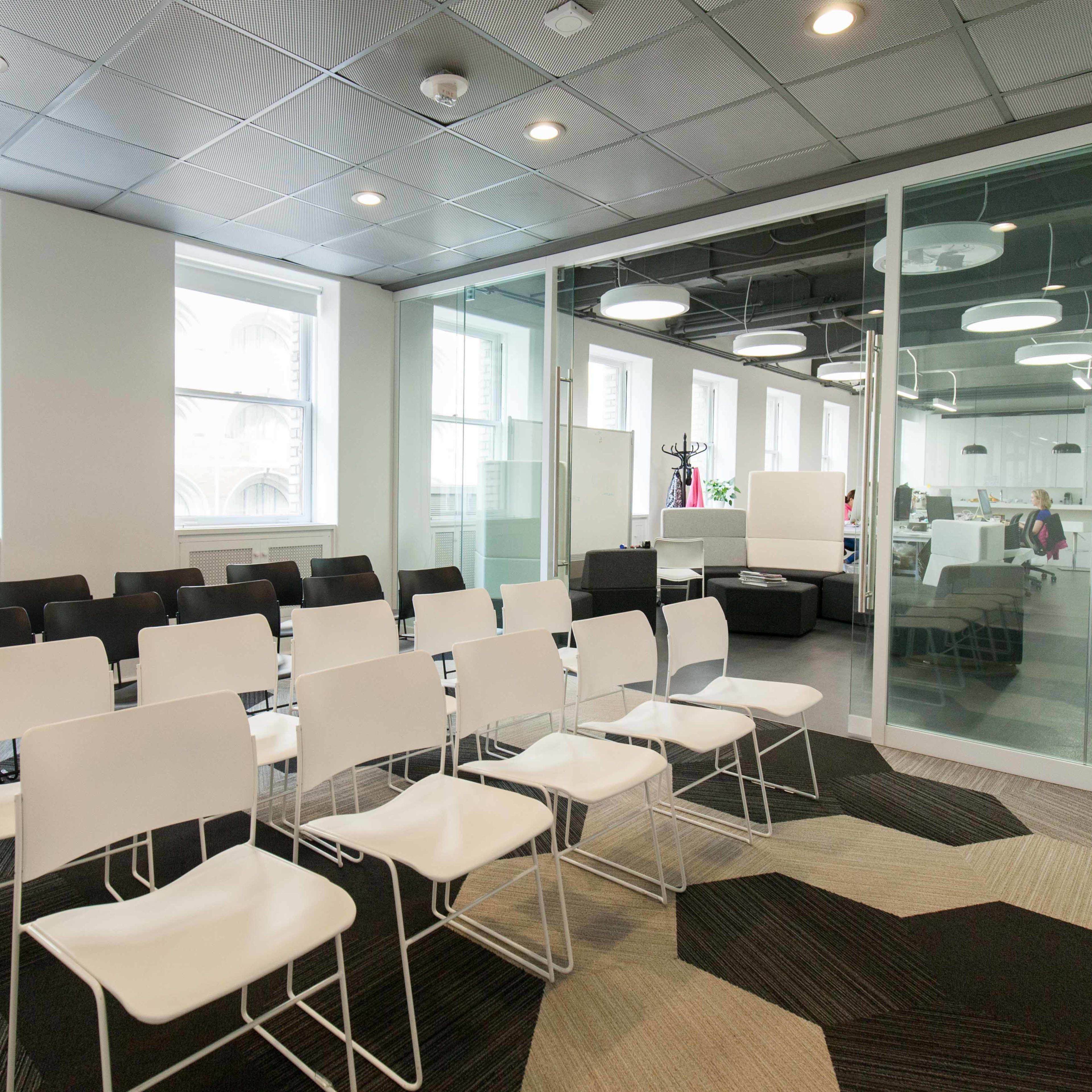 A modern office space features a row of black and white chairs arranged in front of glass partitions and natural light from large windows.