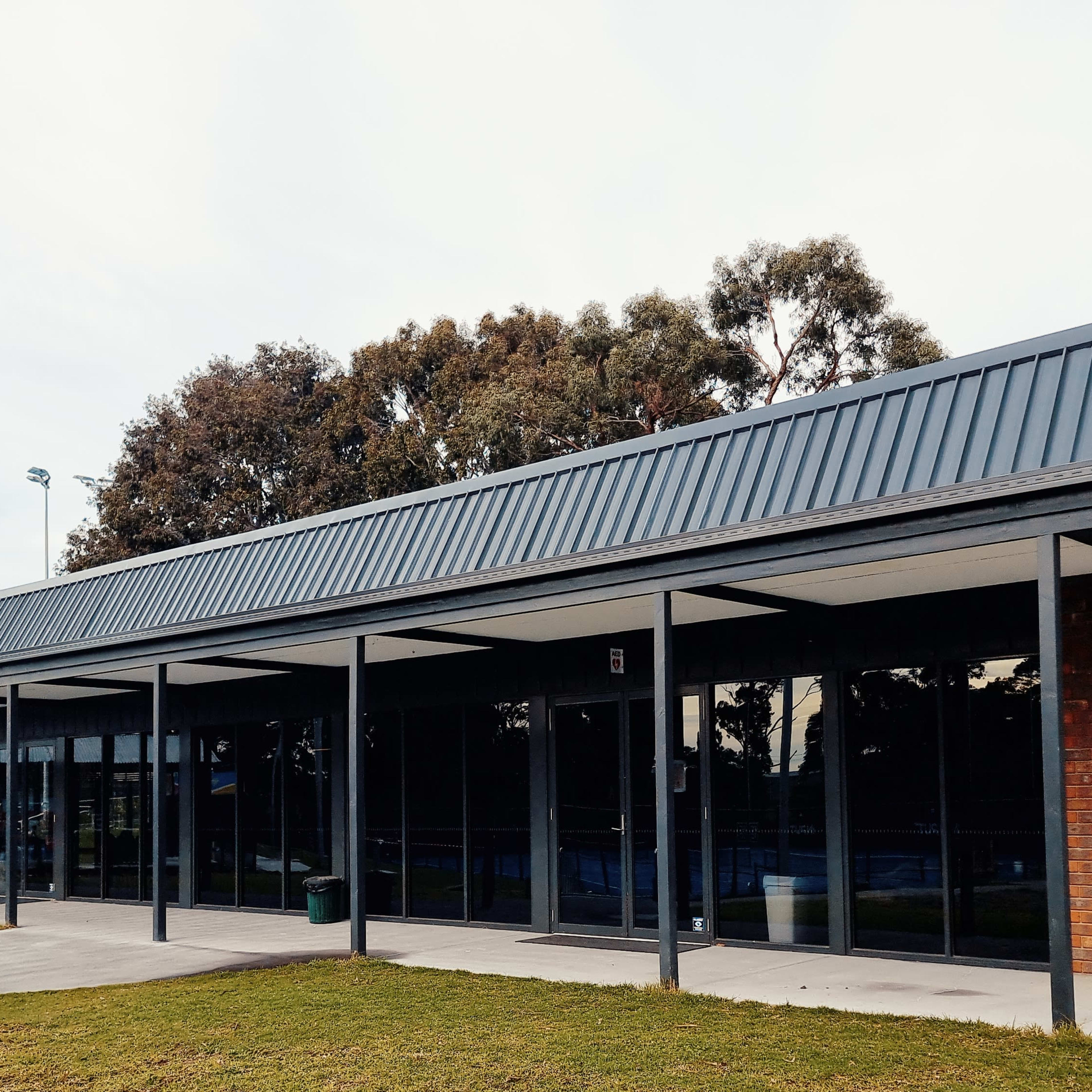 A modern single-story building with a flat roof, large glass windows, and a brick facade, set in a grassy area with a sports court nearby.