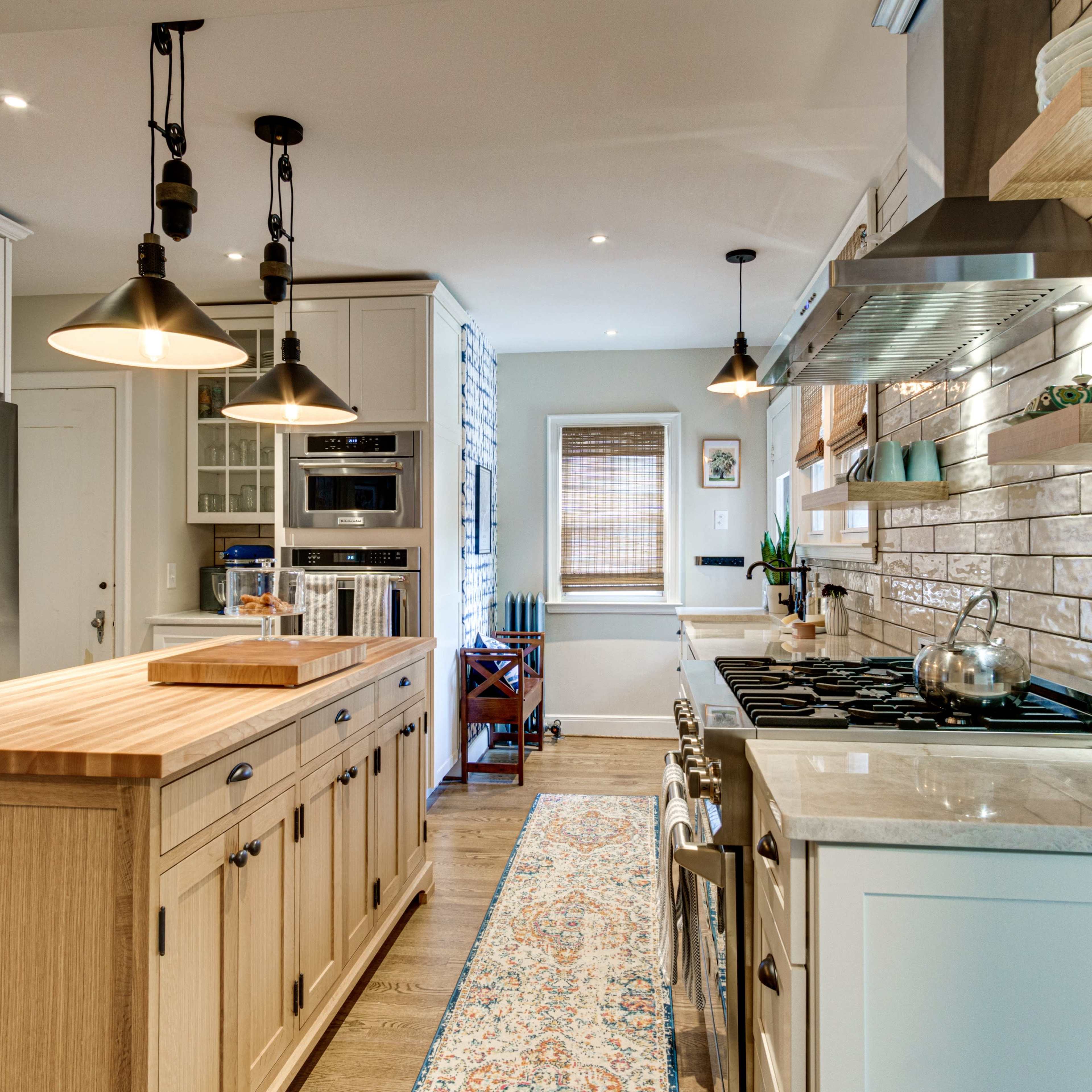 A modern kitchen features a wooden island, stainless steel appliances, and a tile backsplash, illuminated by pendant lights.
