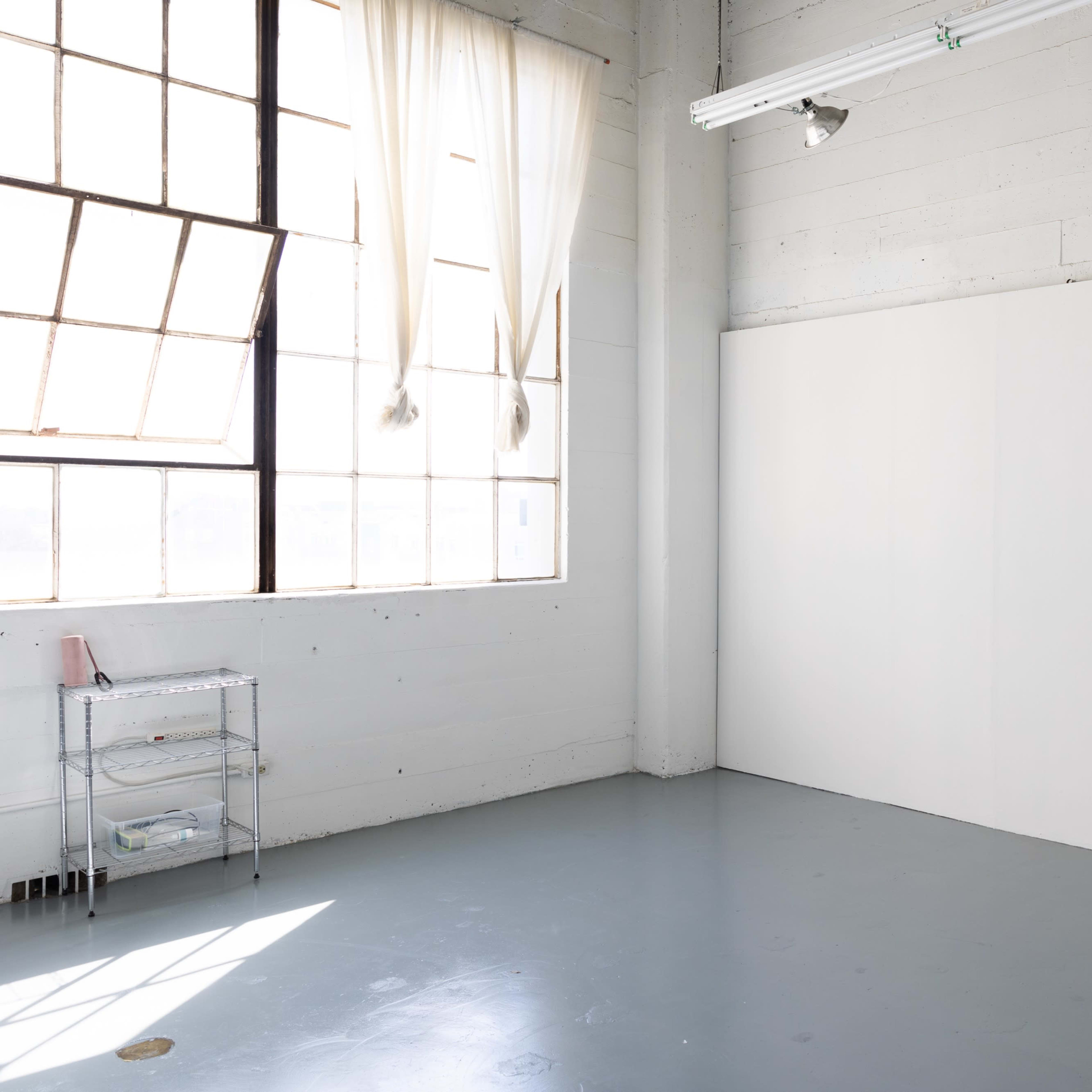A well-lit, empty room with large windows and a blank white wall.