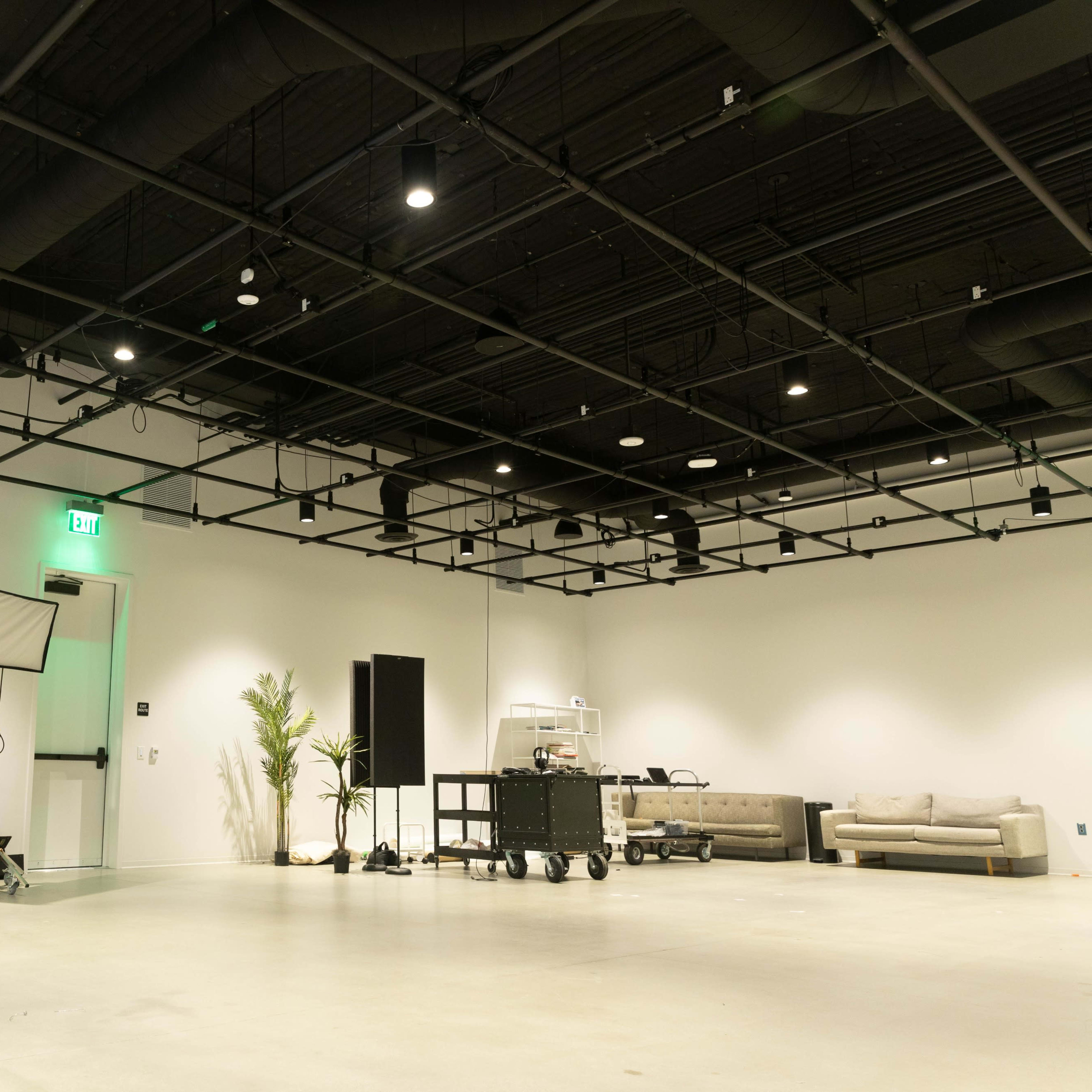 A spacious, well-lit studio with softbox lights, a rolling cart, and a minimalist seating area against a white wall.