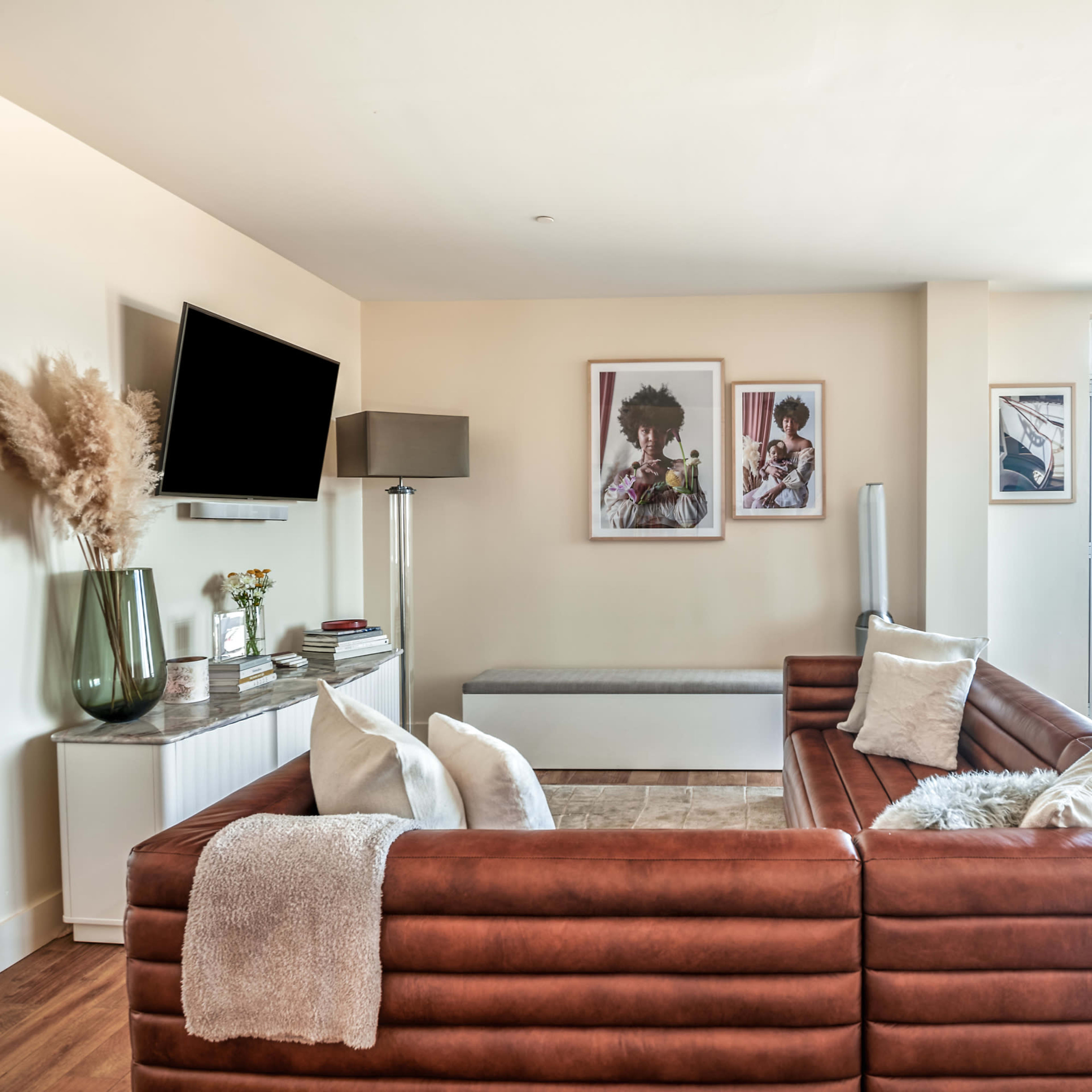 A modern living room featuring a brown sectional sofa, a flat-screen TV mounted on the wall, and large windows with a water view.