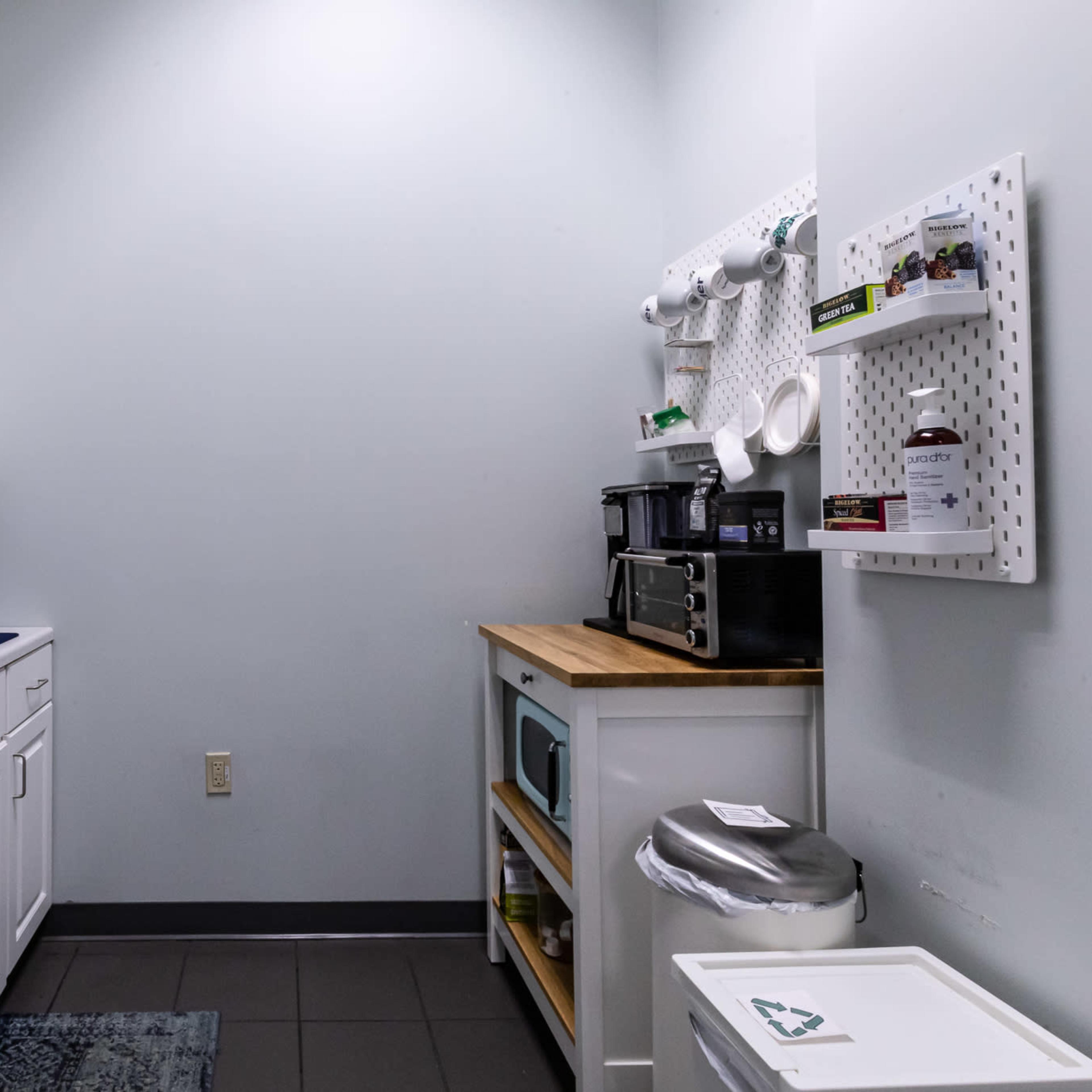 A small kitchen space featuring white cabinetry, a sink, a microwave, a coffee maker, and a trash can.