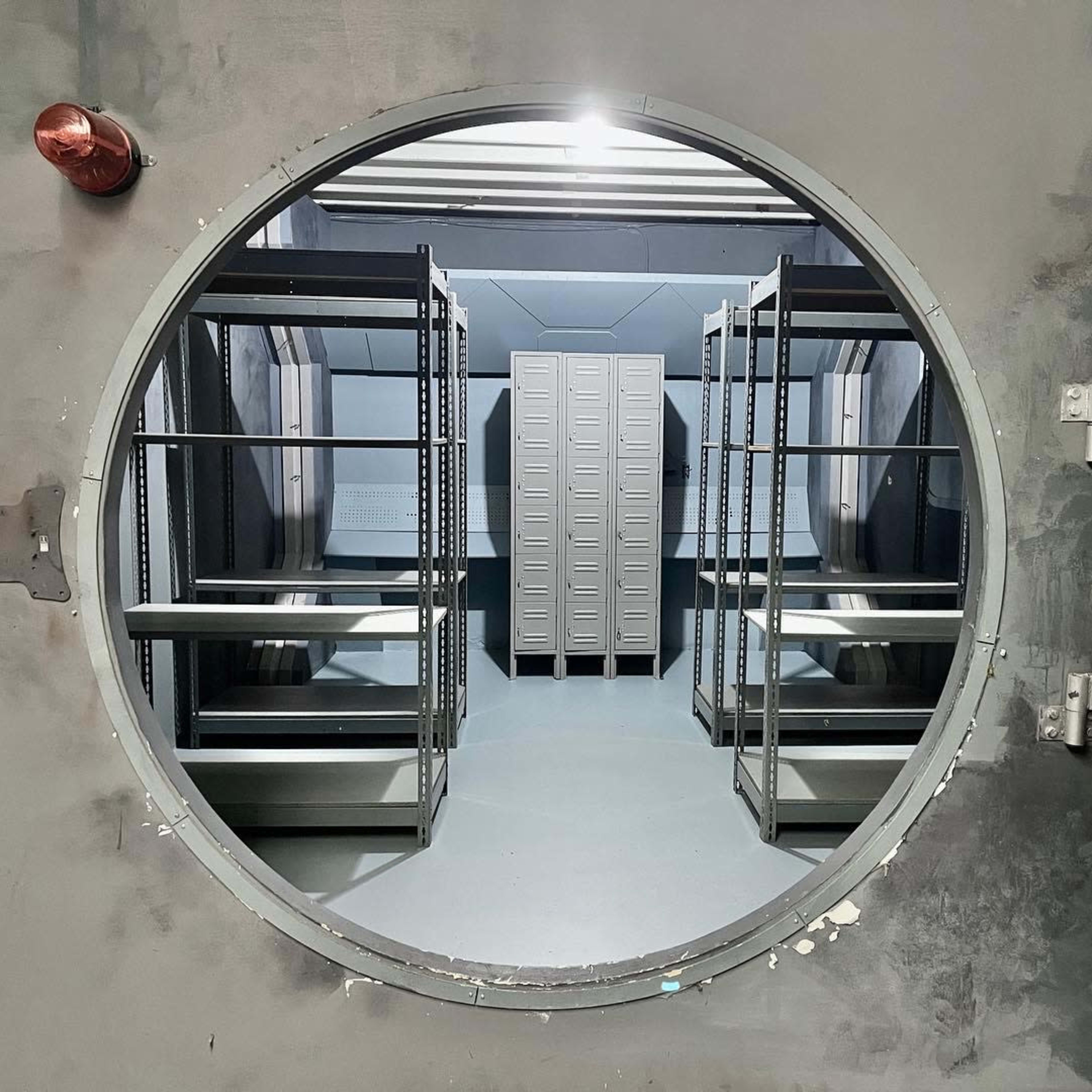 A circular doorway leading into a room with metal shelving units and lockers.