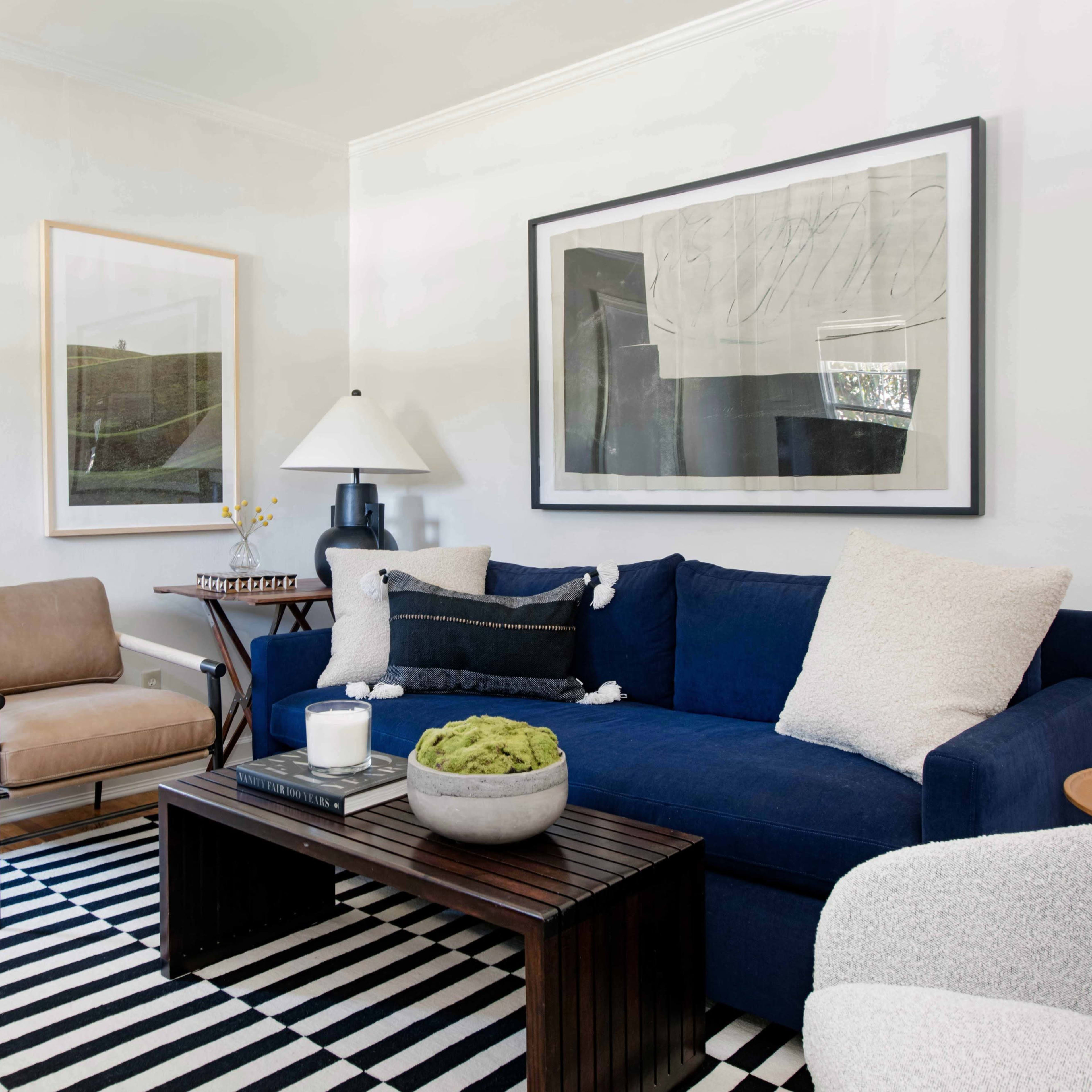 A living room with a blue sofa, a wooden coffee table, an armchair, a lamp, framed artwork on the walls, and a striped rug.